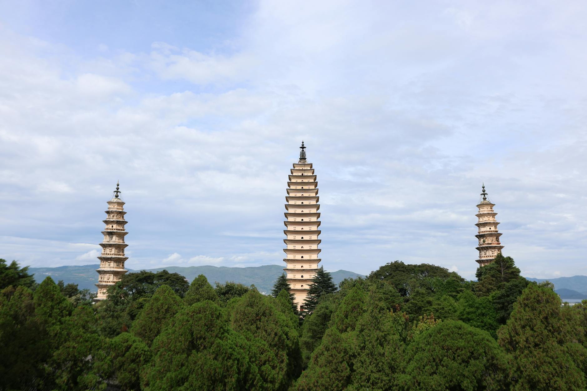 Elegant view of the Three Pagodas in Dali, China, framed by lush greenery and distant mountains.
