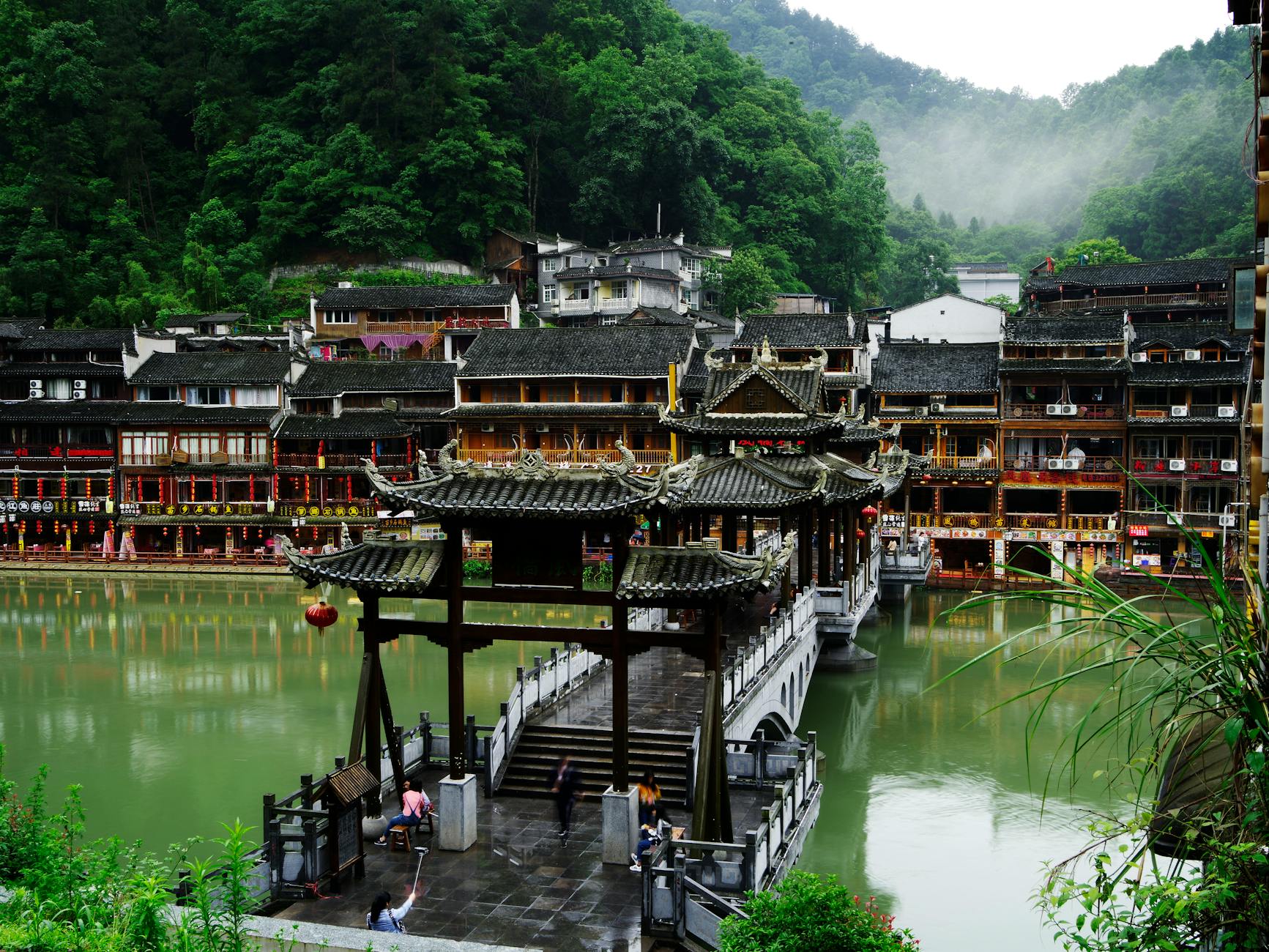 Explore the serene Fenghuang's historic bridge and riverside town under lush greenery.