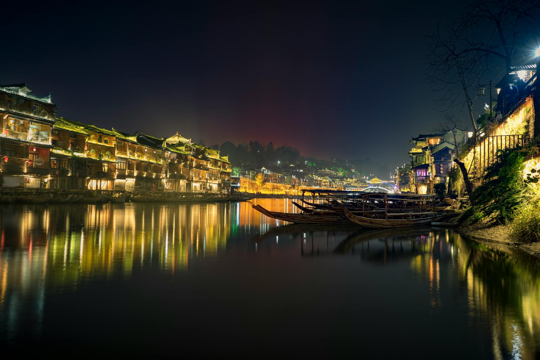 Illuminated Fenghuang Ancient Town with boats on the Tuo River at night