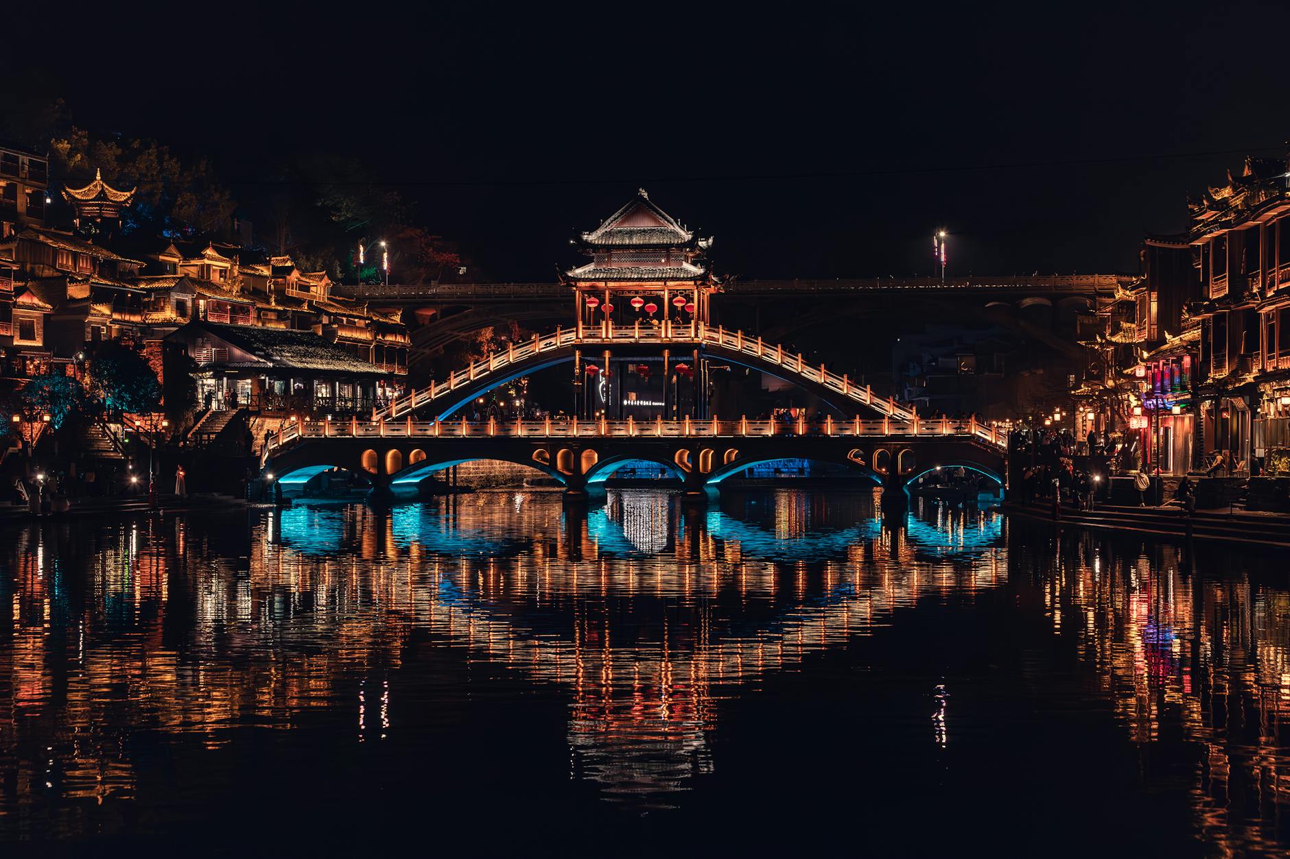 Stunning night view of Fenghuang Bridge in Xiangxi, China, with vibrant reflections.