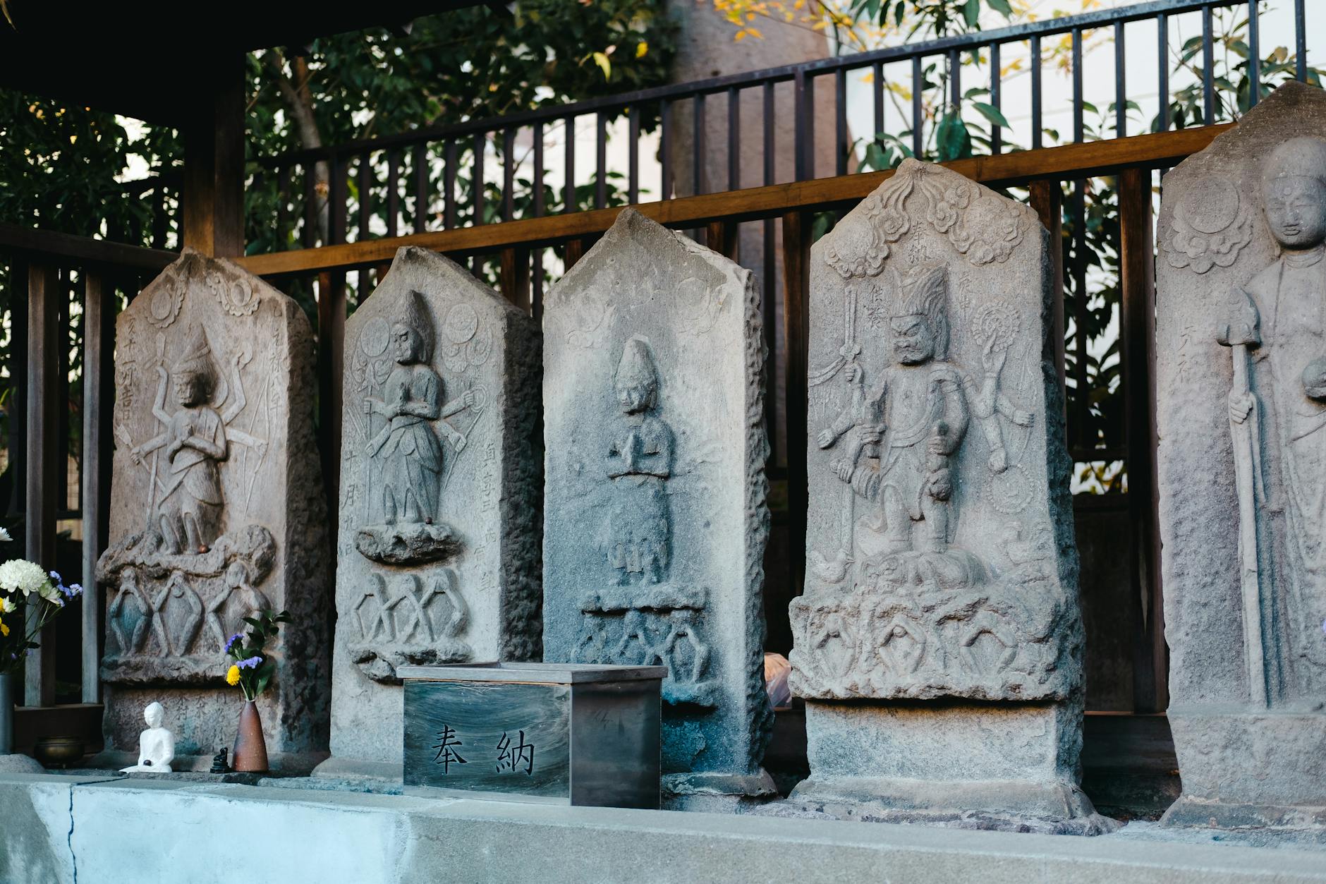 Ancient stone steles with detailed carvings in a tranquil Japanese temple setting.