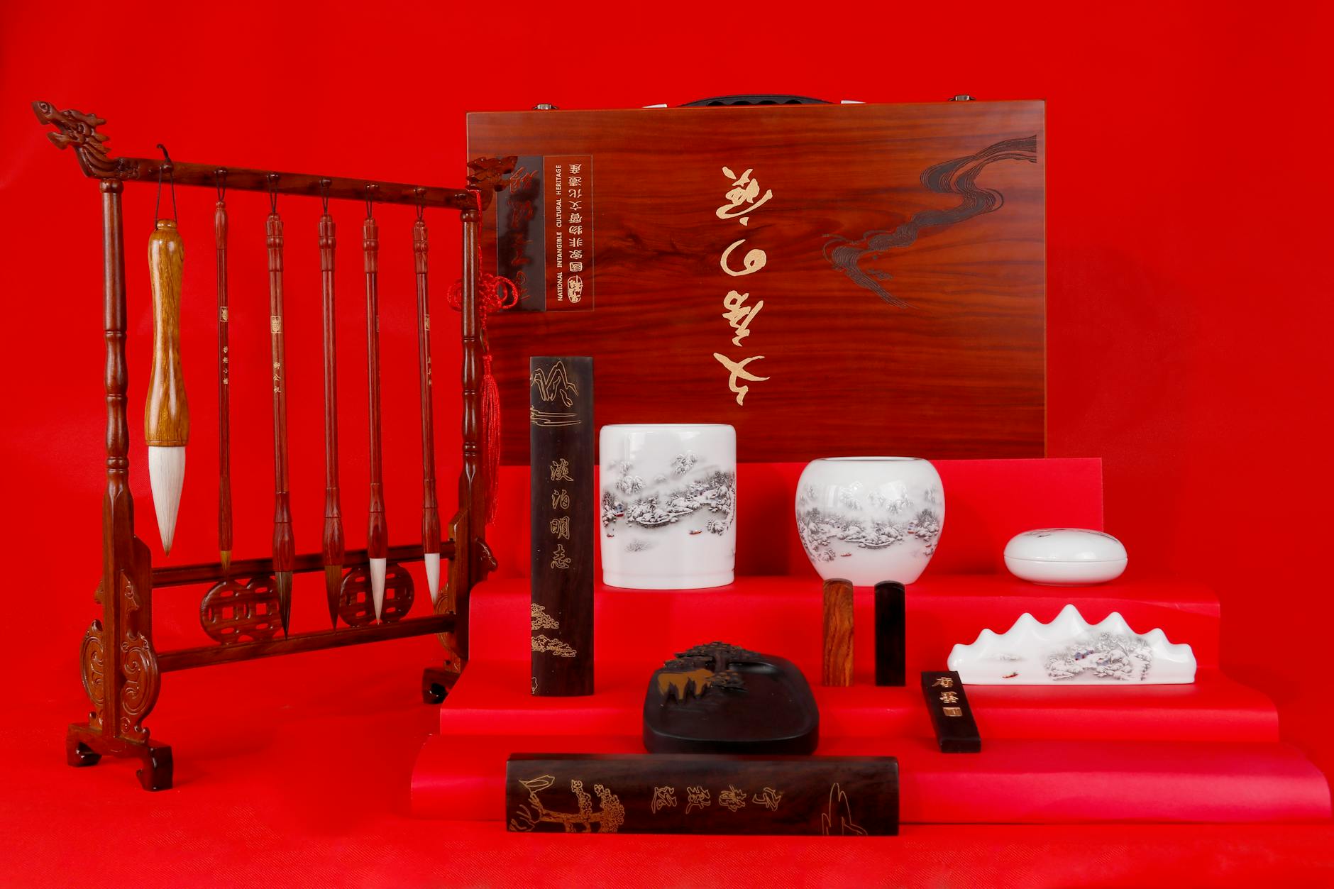 A visually striking set of traditional Chinese calligraphy tools on a vibrant red background.