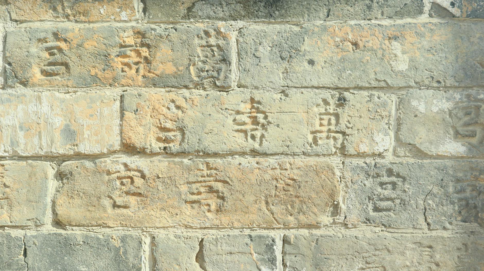 Close-up of an ancient stone wall with Chinese inscriptions, showcasing historic architecture.