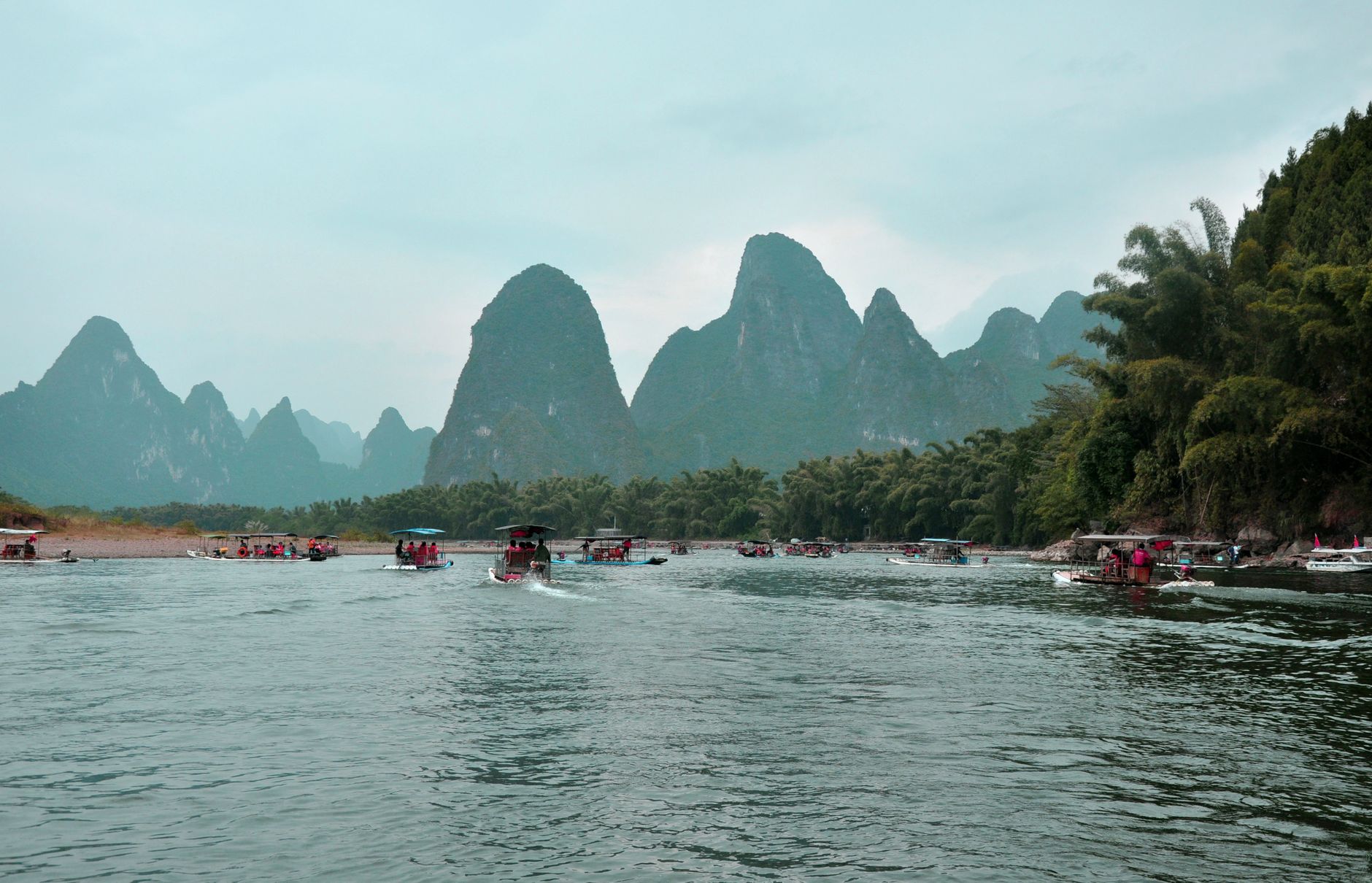 A serene view of the Li River with karst mountain backdrop and boats in Yangshuo, China.