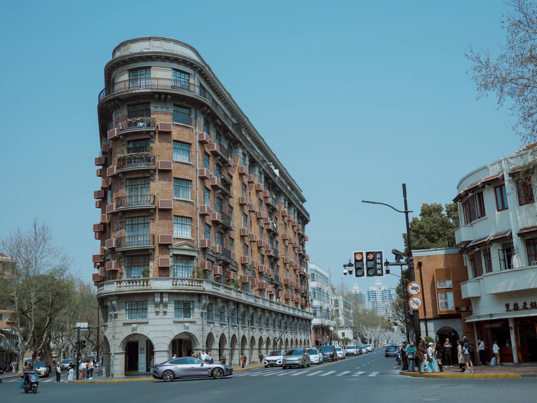 Historic corner building on a bustling street with urban traffic and pedestrians under a clear blue sky.