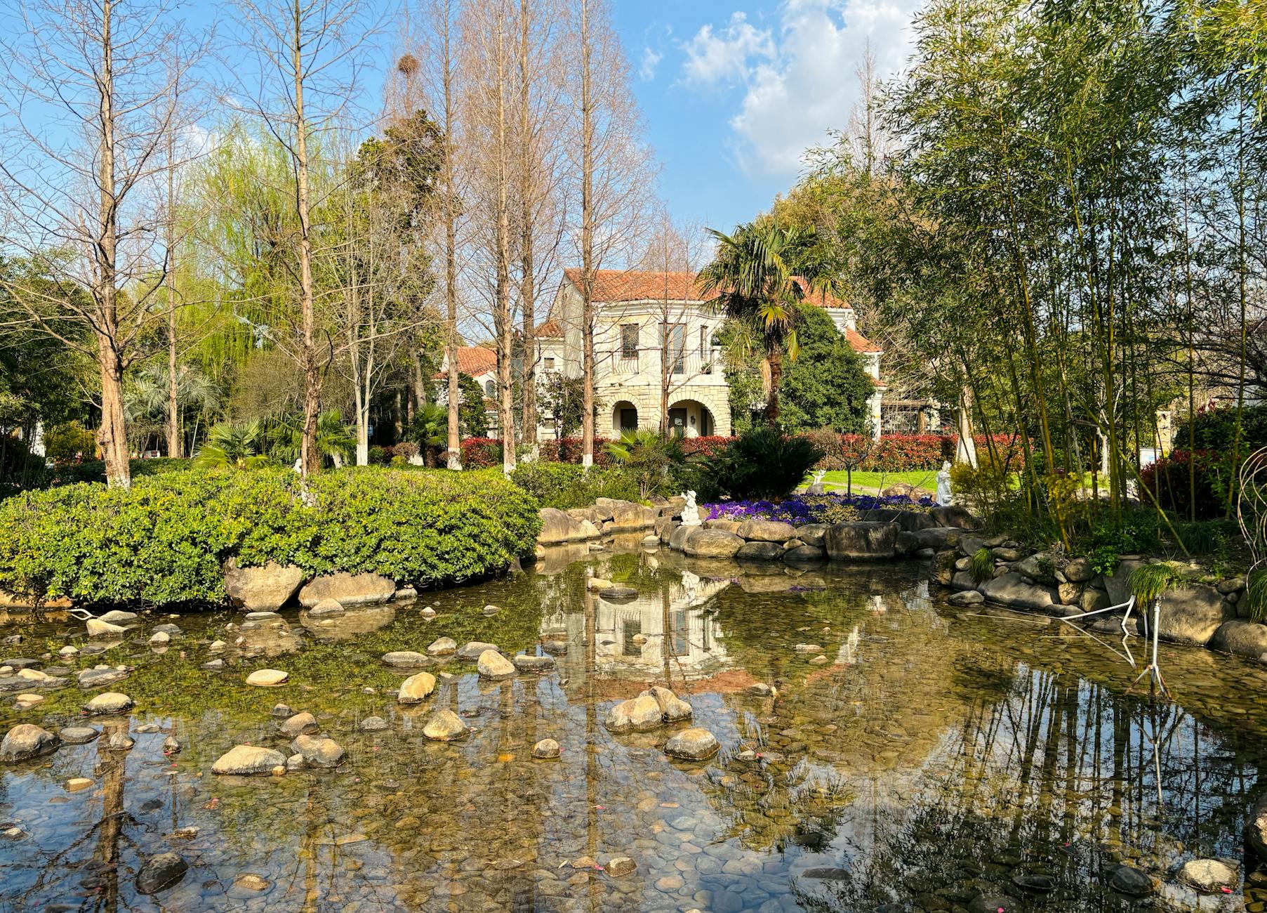 Scenic view of a serene park with a pond, trees, and a charming house in the background.