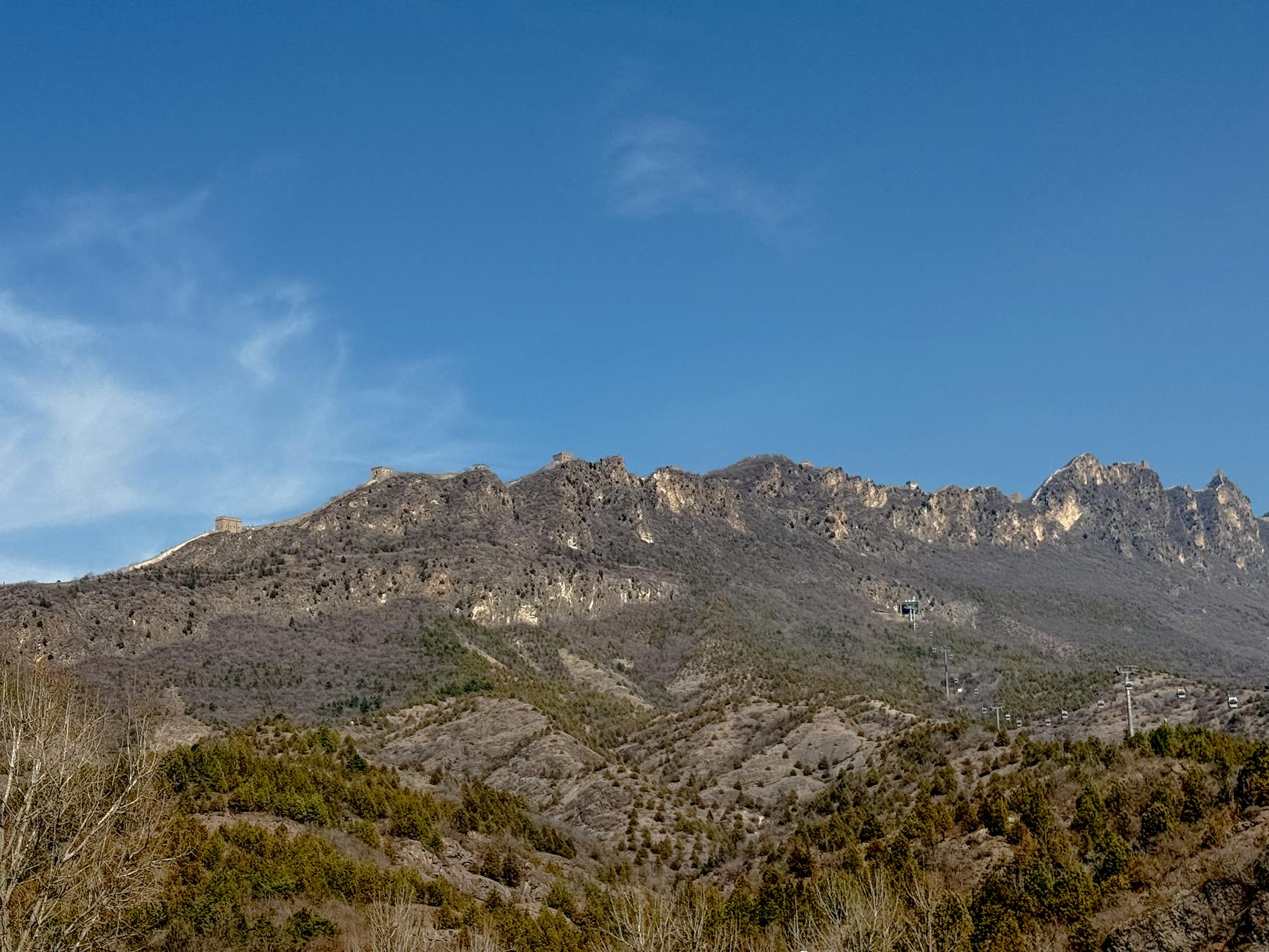 Experience the grandeur of the Great Wall amidst China's stunning mountainous terrain under a clear blue sky.
