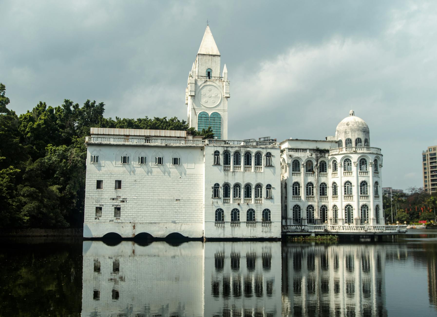 Elegant white building with clock tower reflecting on a tranquil lake in Guangzhou.