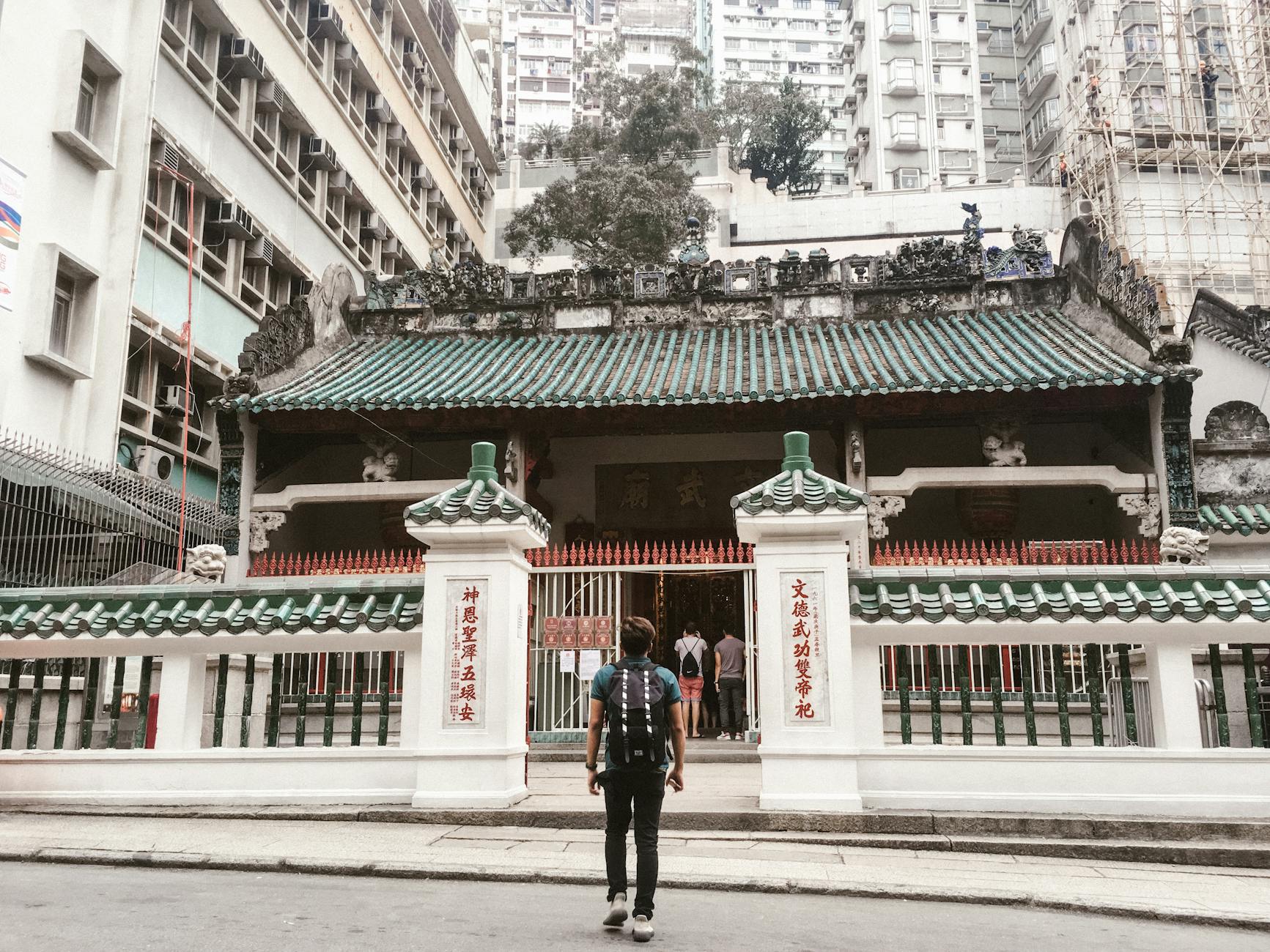 Backpacker visiting the historic Man Mo Temple on Hong Kong Island, surrounded by skyscrapers.
