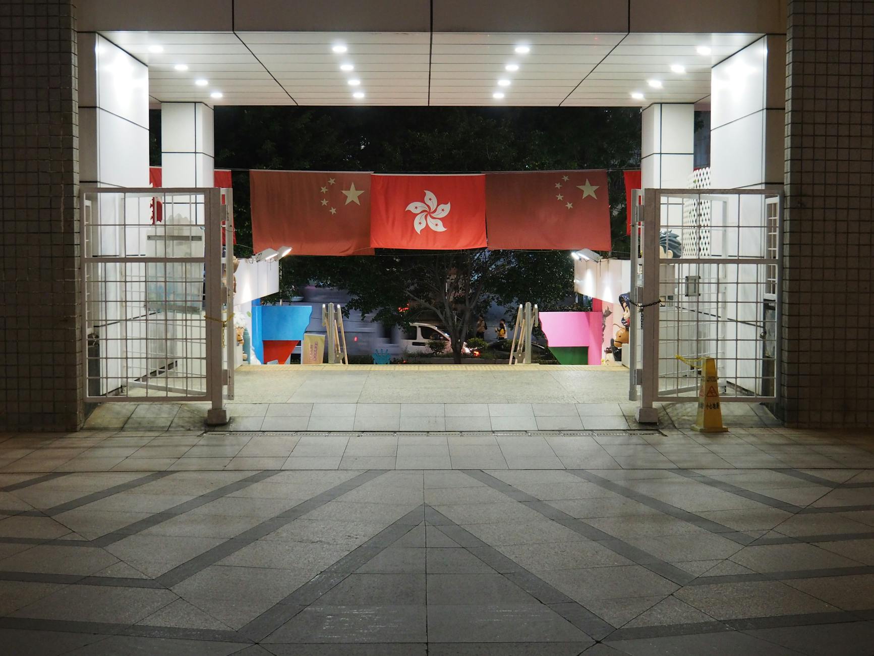 A nighttime view of a Hong Kong entrance with hanging flags prominently displayed.