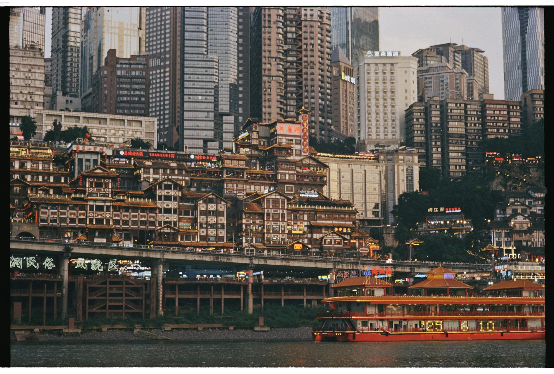 Colorful Chongqing buildings and riverboat illuminate the night, showcasing urban vibrancy.