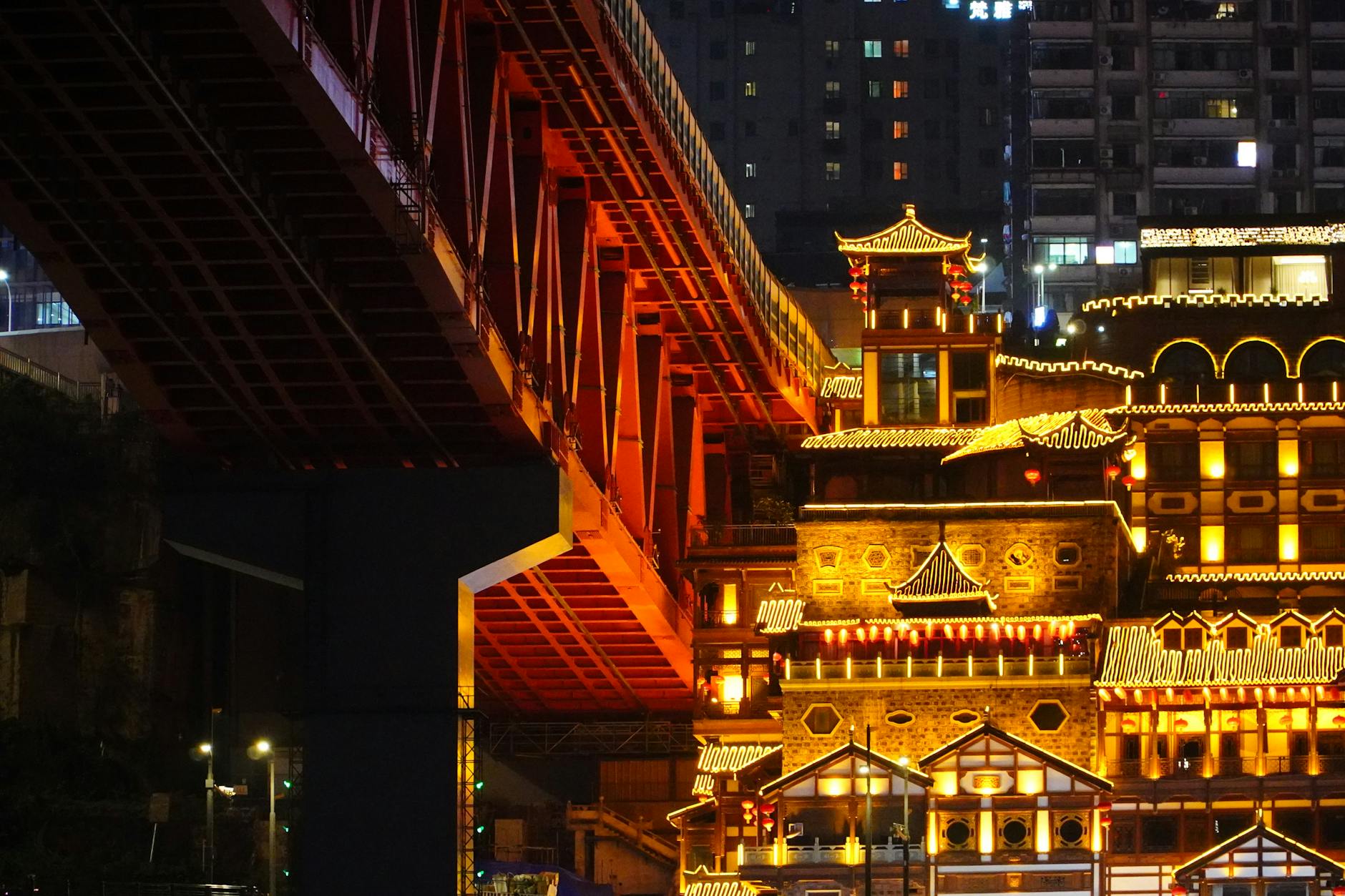 Night view of a beautifully lit traditional building under a modern urban bridge.