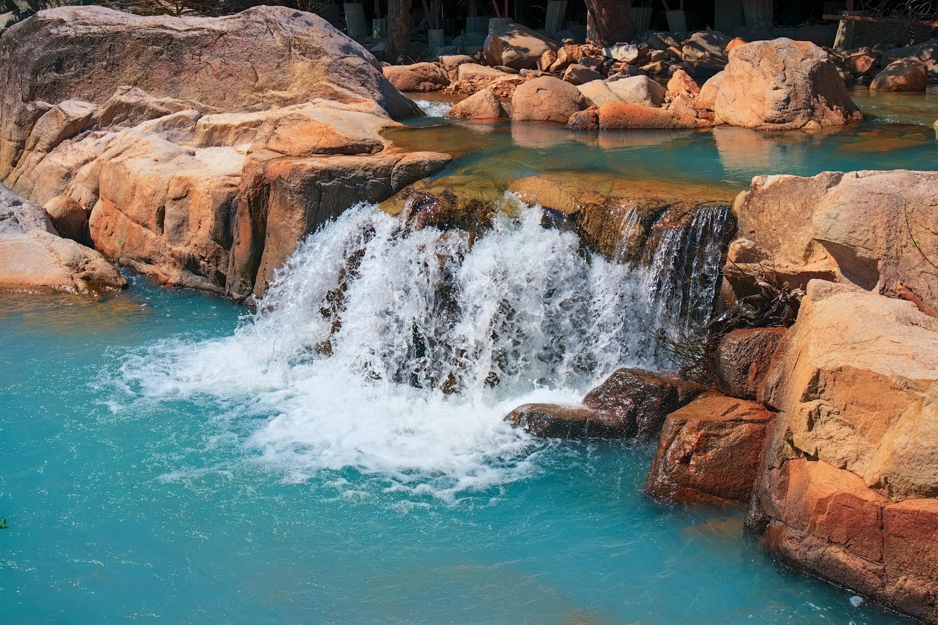 Peaceful waterfall flows over rocks into a turquoise pool in a natural setting.