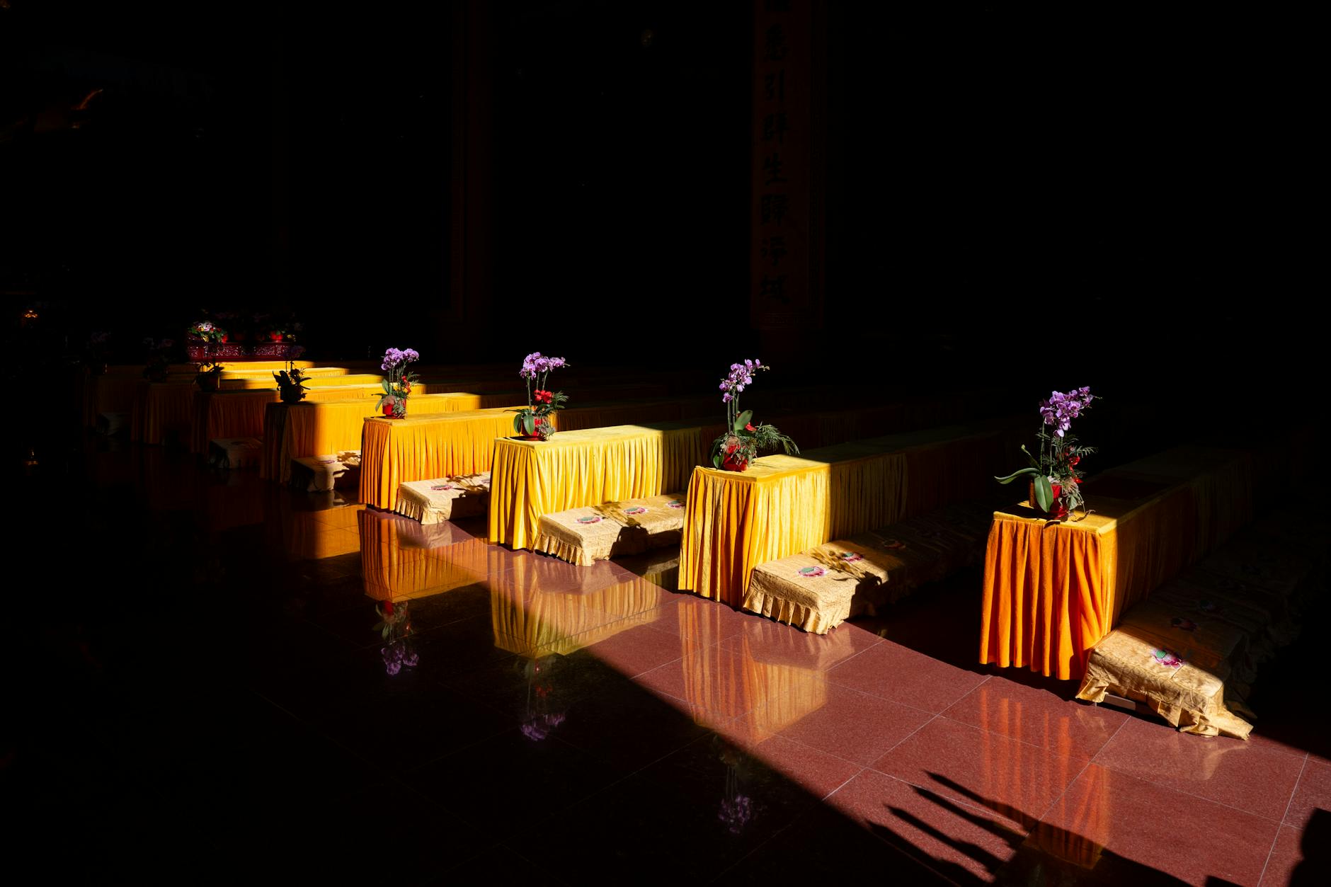 A row of altars with yellow cloths and flowers in sunlight at a temple in Shanghai, China.