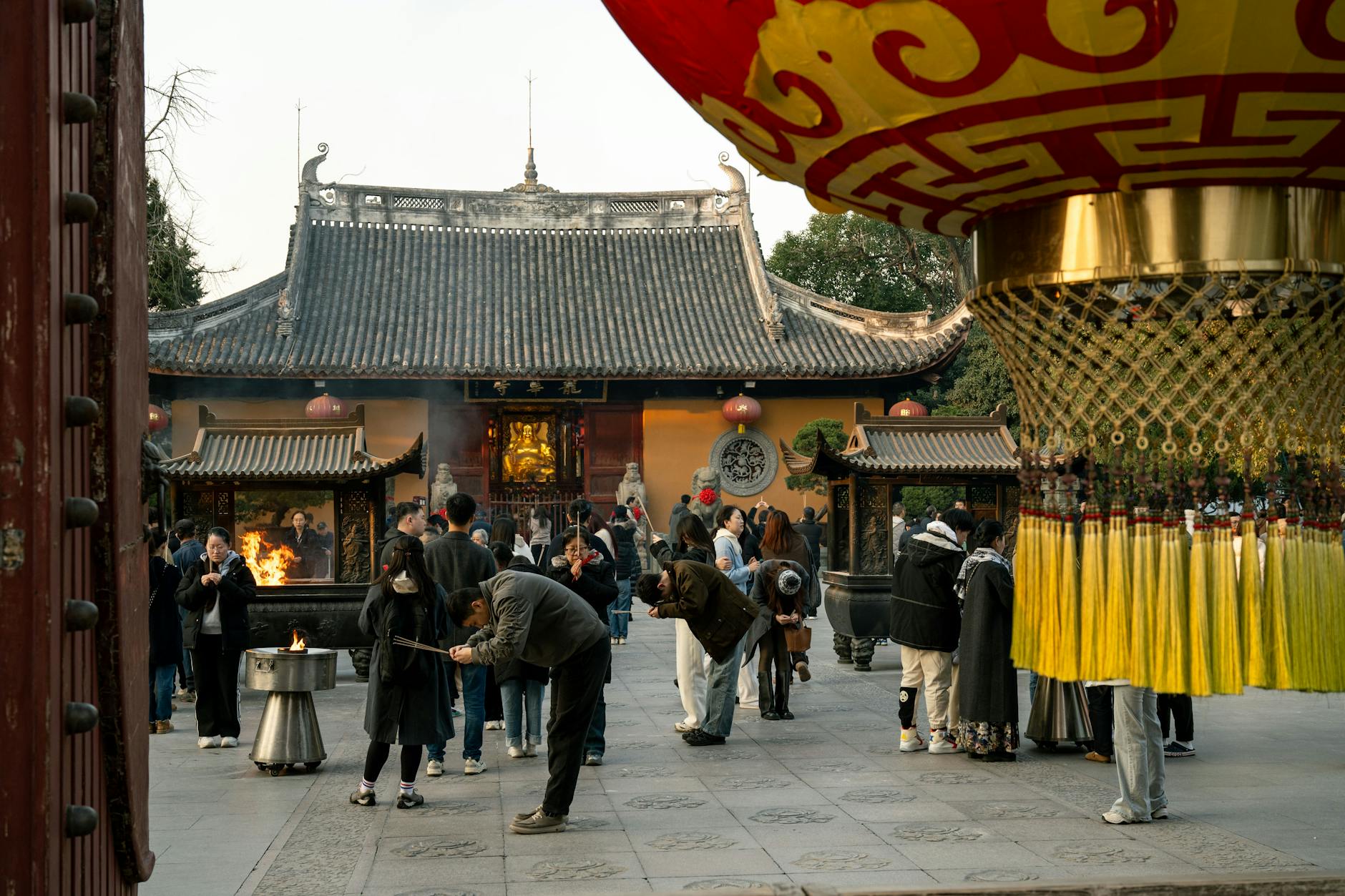 A bustling temple courtyard in Shanghai, with people engaged in rituals and vibrant decorations.