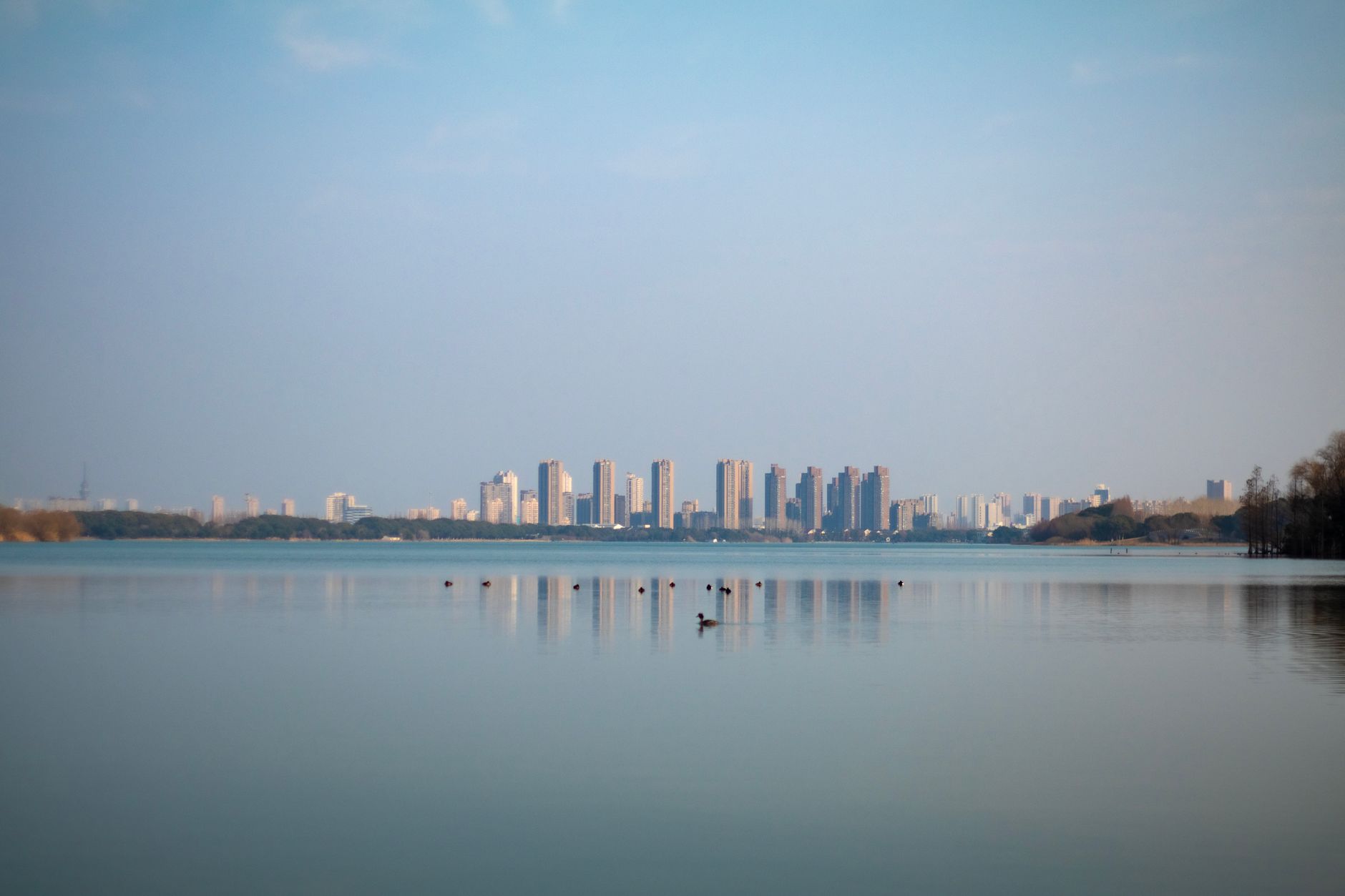Tranquil lake with city skyline in Suzhou, China, reflecting buildings.