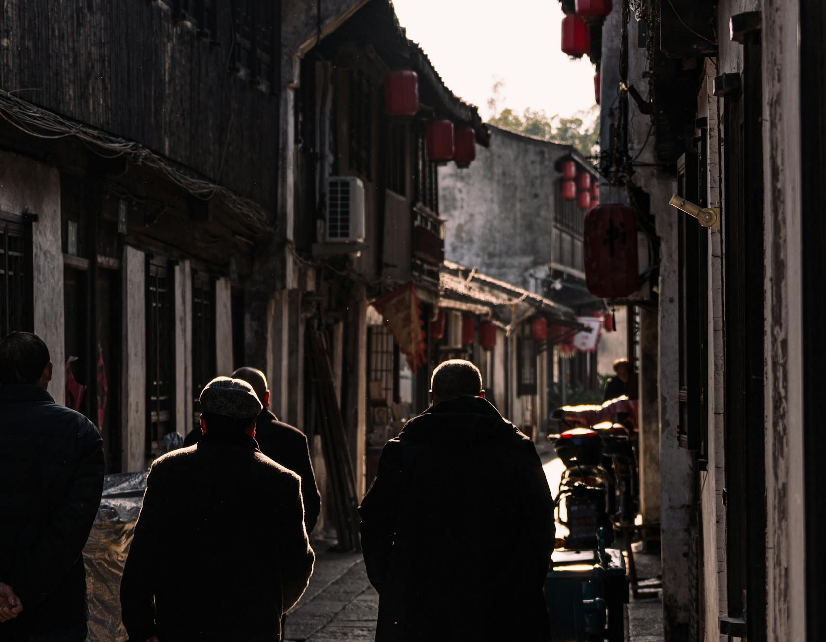 Silhouetted figures walking through traditional Asian alley with red lanterns.