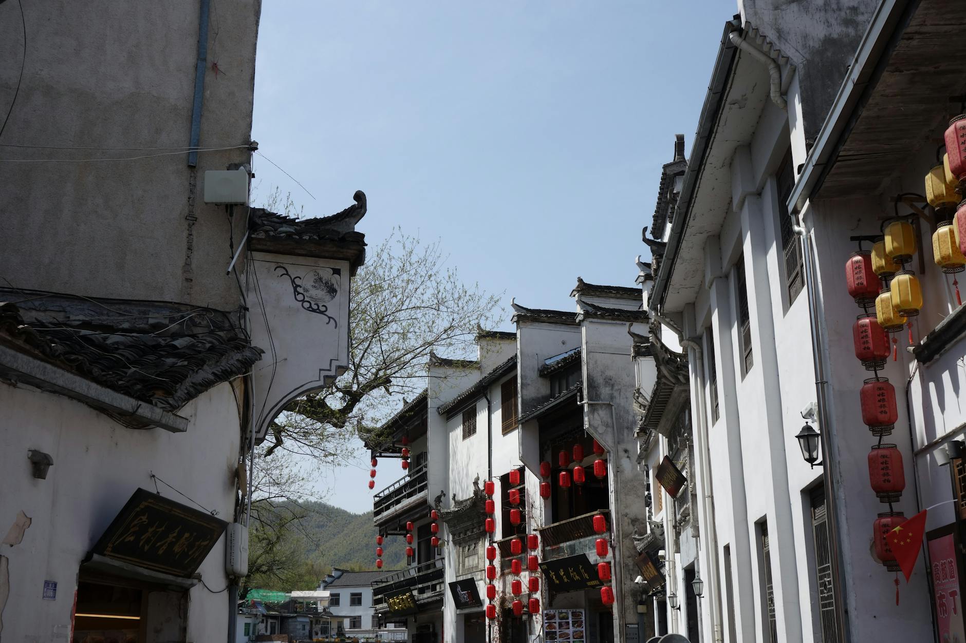 Quaint street in traditional Chinese architecture with red lanterns under a clear blue sky.