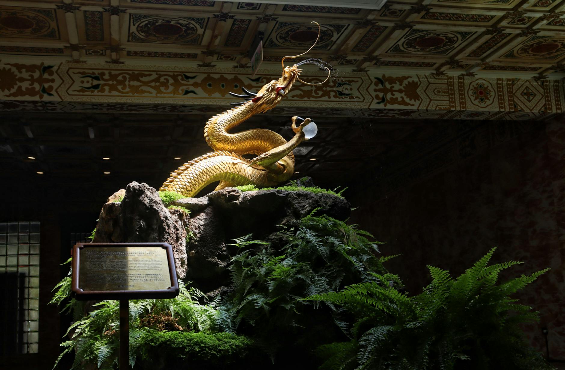 Gold dragon sculpture displayed on a rocky base indoors with ornate ceiling details.