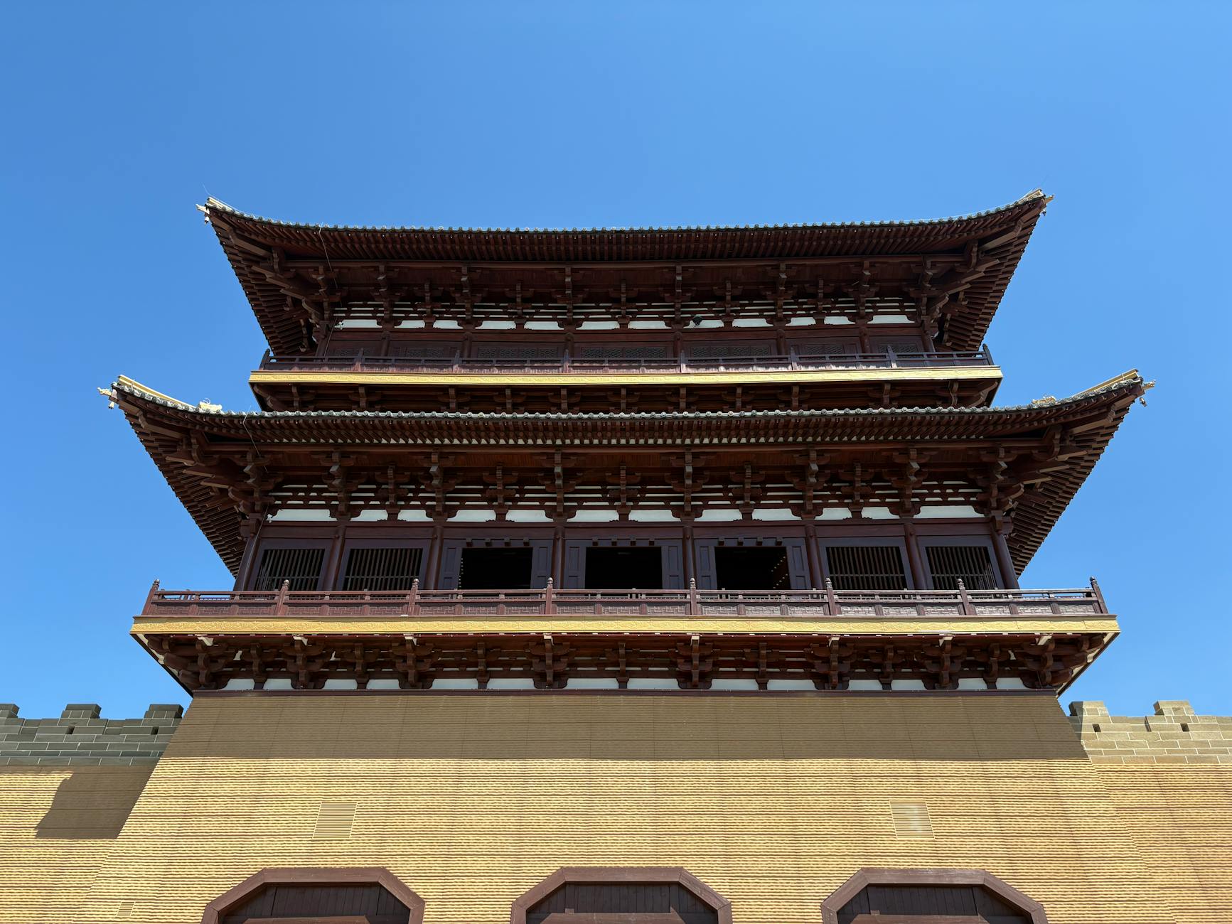 Upward view of a traditional Chinese tower with intricate wooden architecture under a clear blue sky.