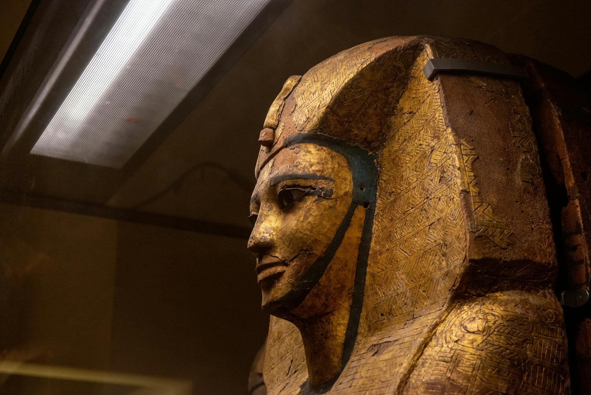 Close-up of a golden Egyptian pharaoh mask displayed in a museum setting.