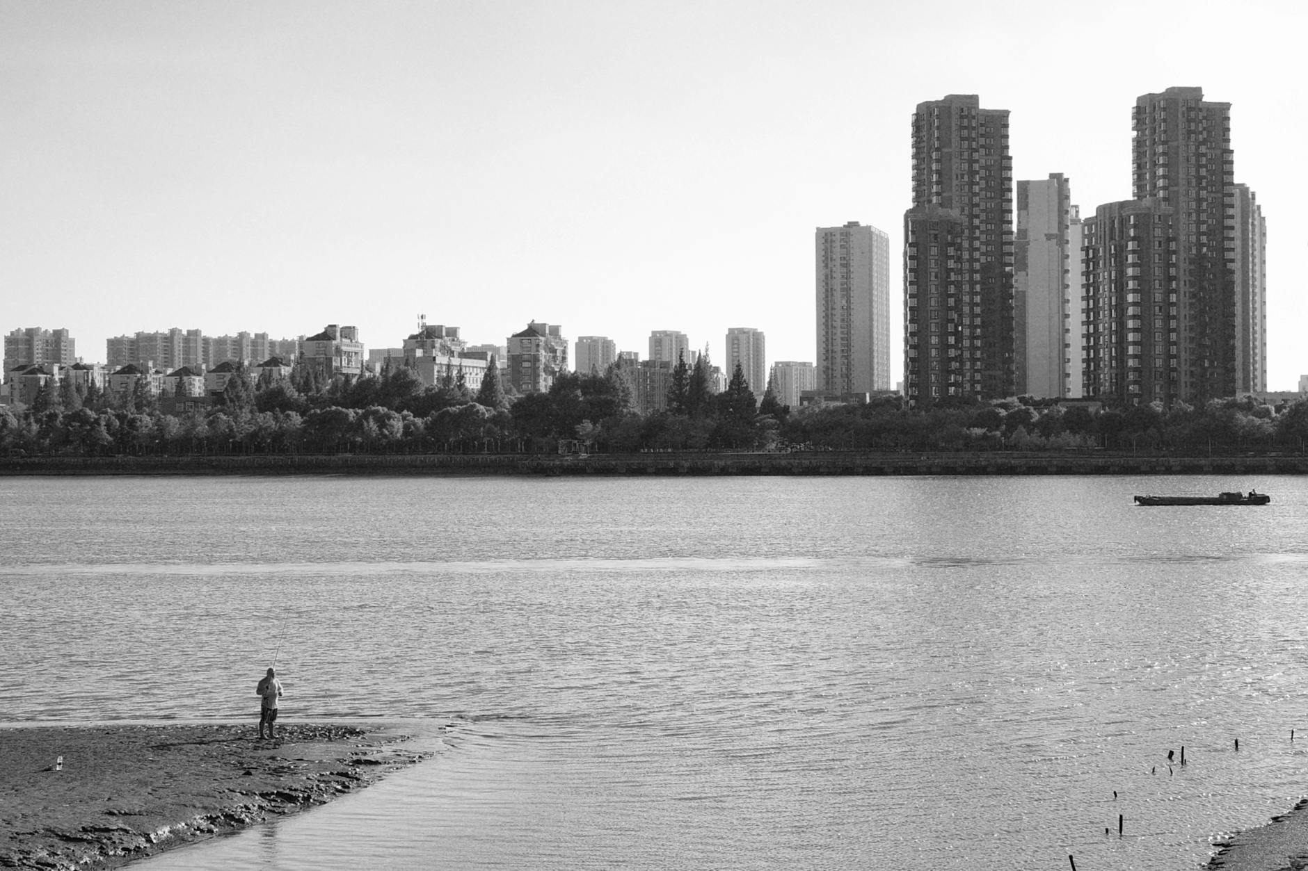 Monochrome view of Shanghai's skyline with waterfront and distant high-rise buildings.