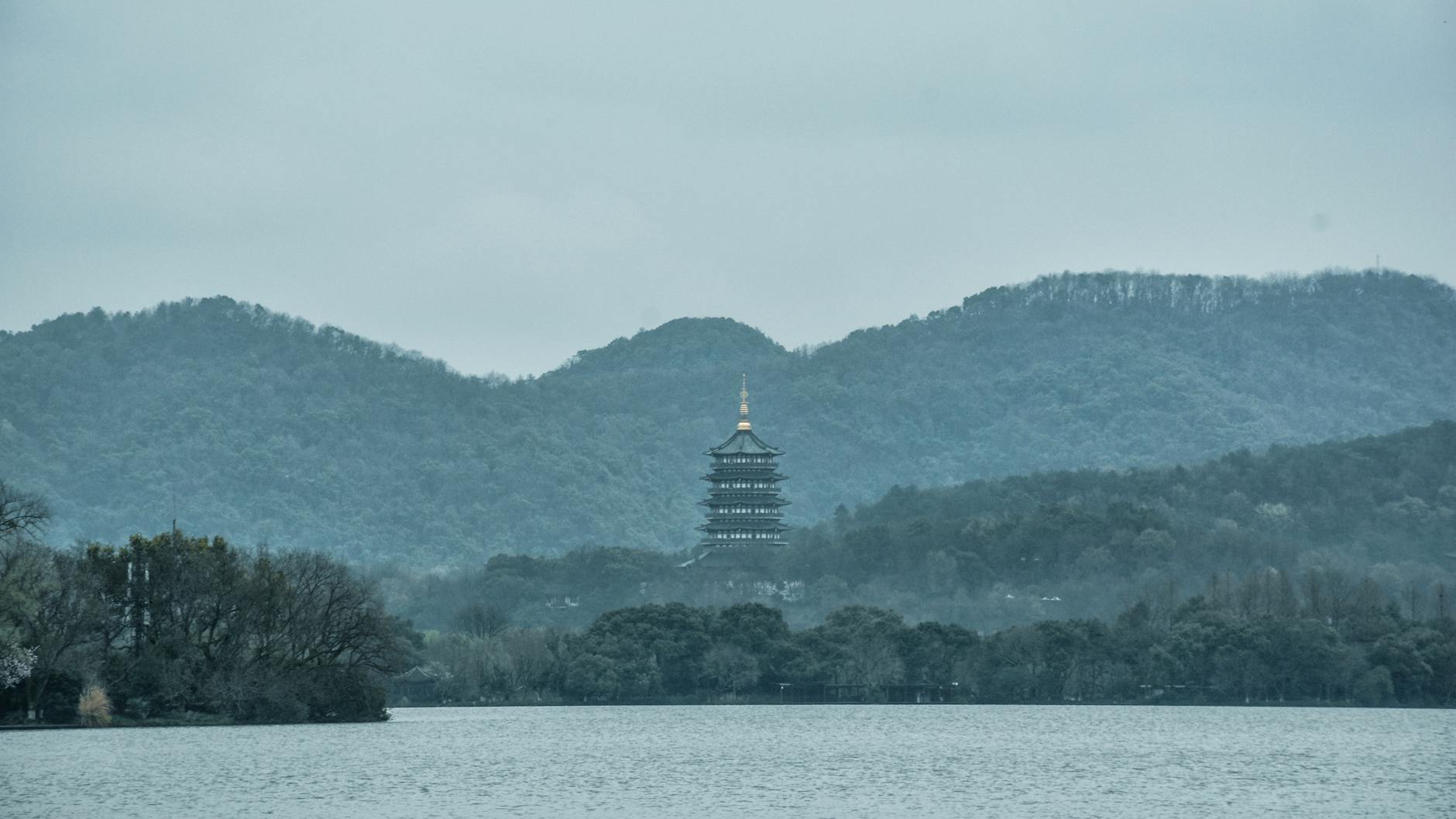 Tranquil scene featuring a pagoda surrounded by lush mountains and a peaceful lake.