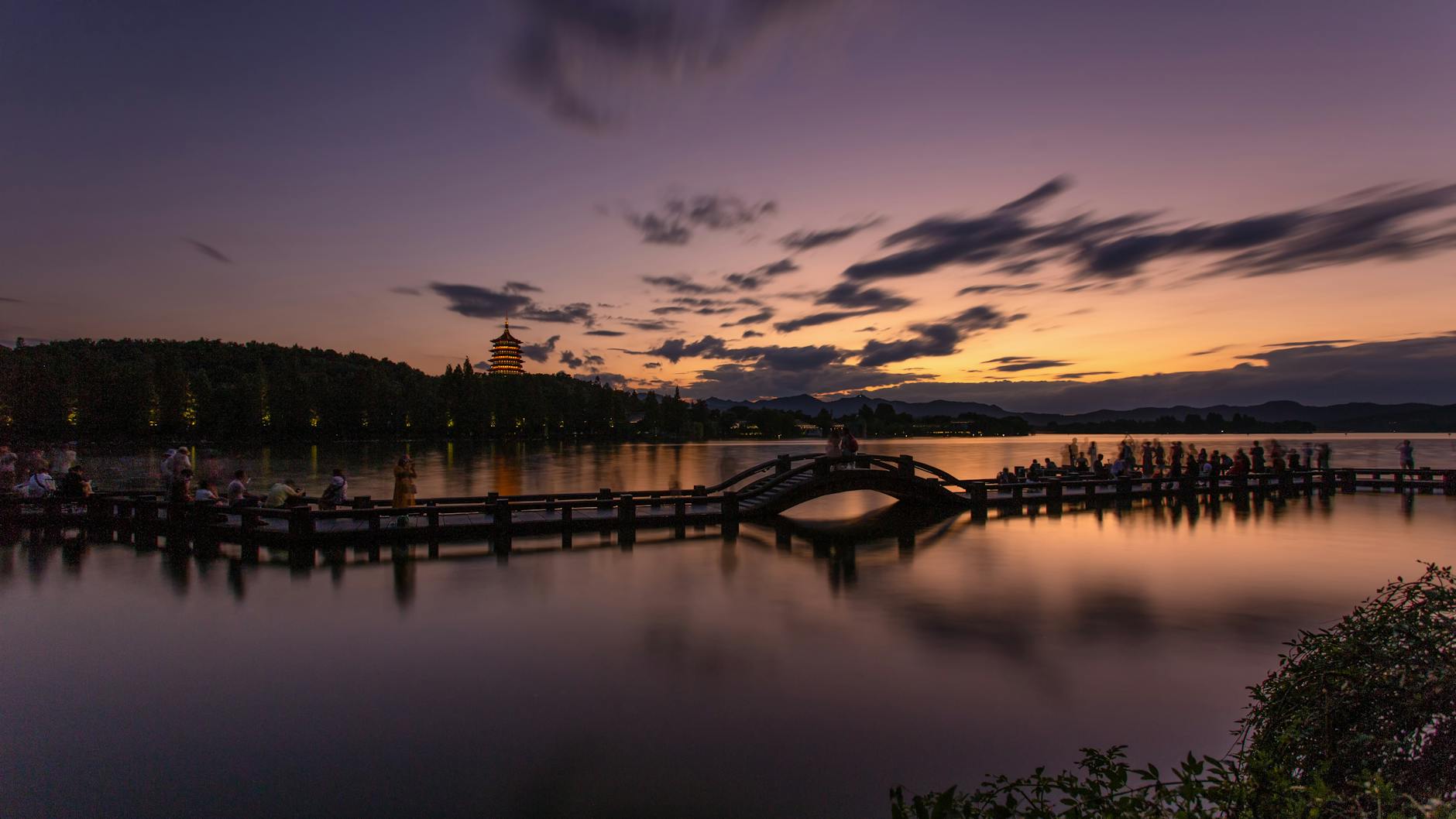 Serene twilight scene of West Lake in Hangzhou, showcasing a silhouetted pier and pagoda.