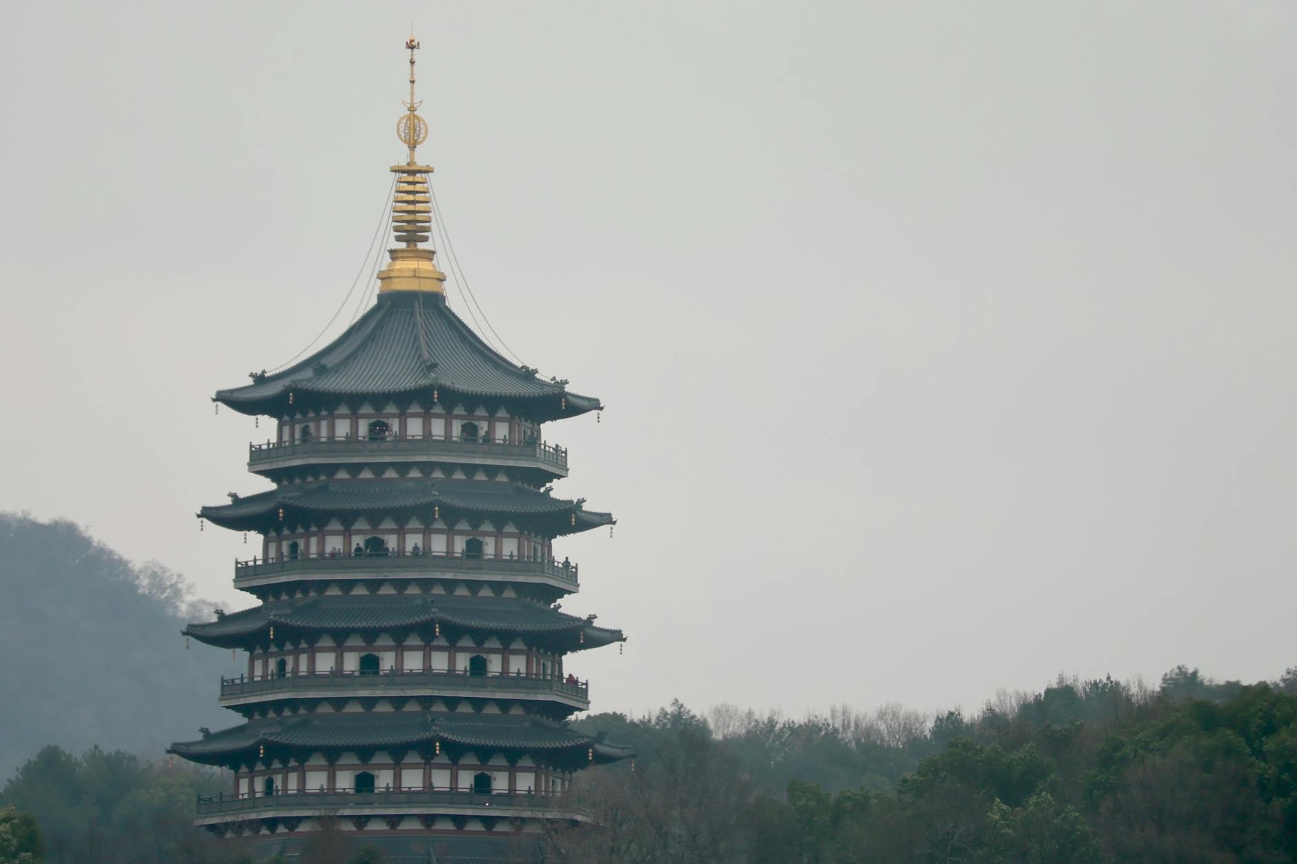 Leifeng Pagoda in Hangzhou surrounded by lush greenery on a misty day.