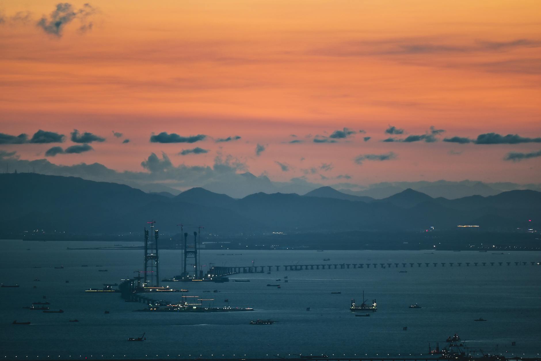 View of Shenzhen Bay Bridge at sunset with vibrant sky and distant mountains.