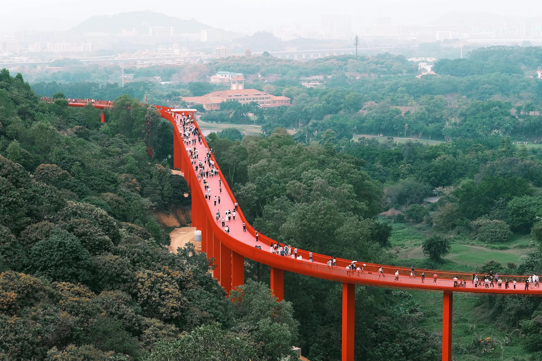 A vibrant red bridge stretches over lush green landscapes in Shenzhen, China, capturing a lively scene.