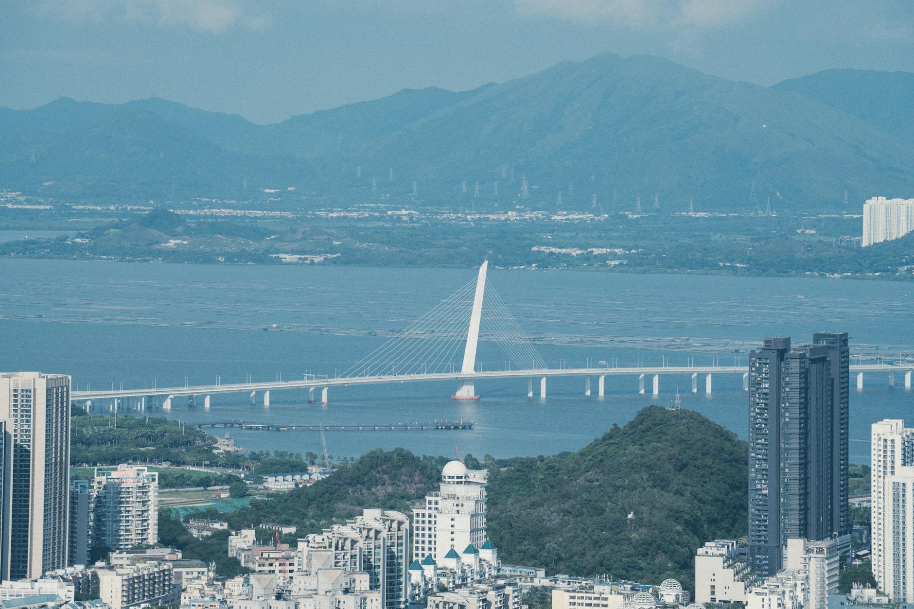 Captivating aerial view of Shenzhen Bay Bridge with towering skyscrapers and mountain backdrop.