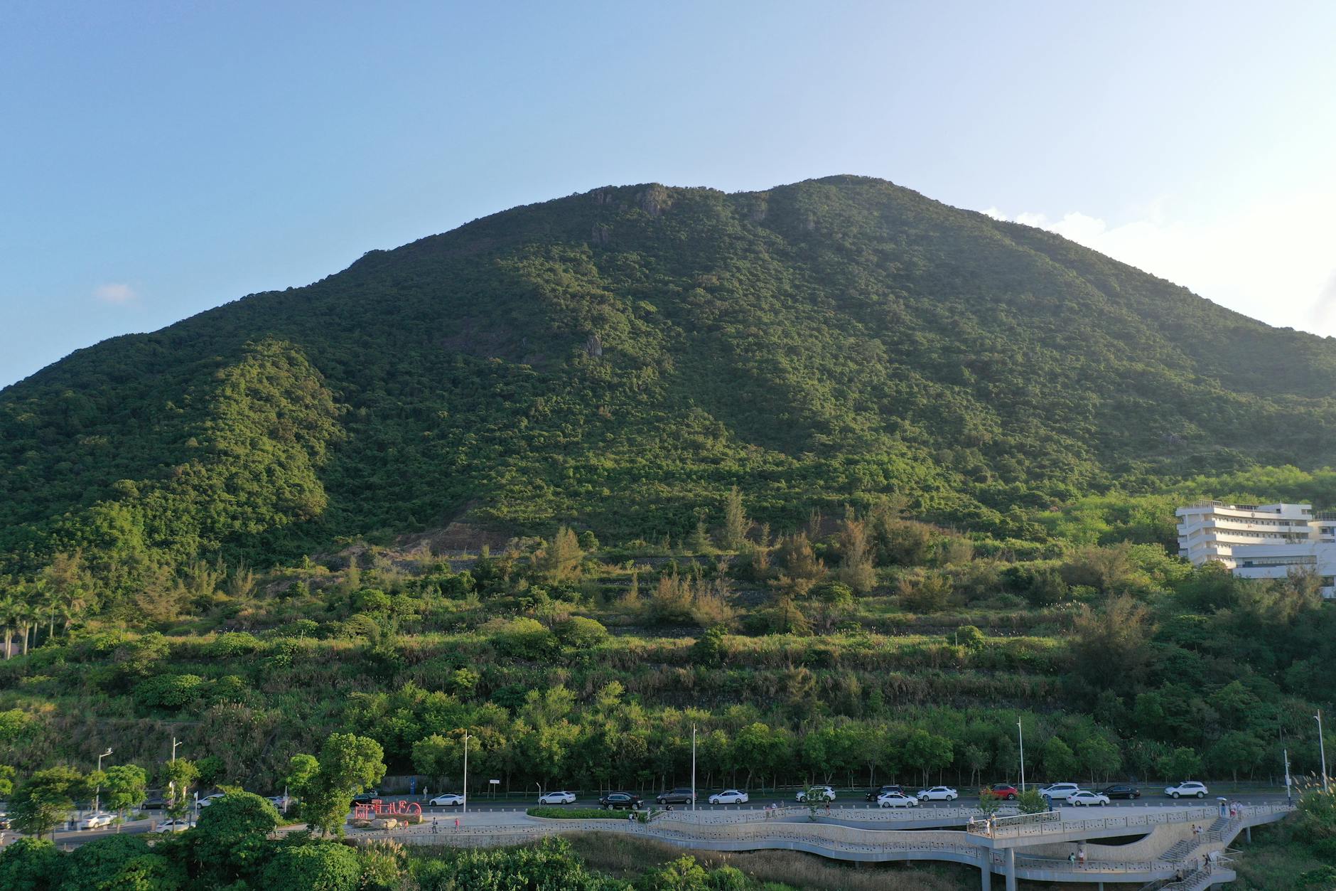 High aerial drone view of a green mountain landscape in Shenzhen, showcasing natural beauty and urban infrastructure.