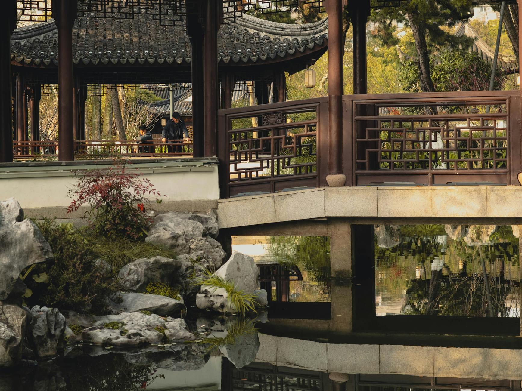 A tranquil scene of a classical garden pavilion and footbridge reflecting in a calm pond.
