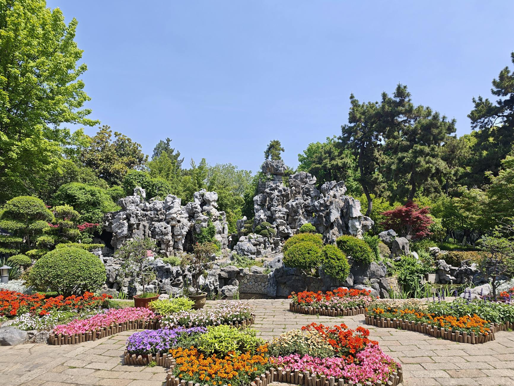 Vibrant garden showcasing diverse plants and striking rock formations under a clear sky.