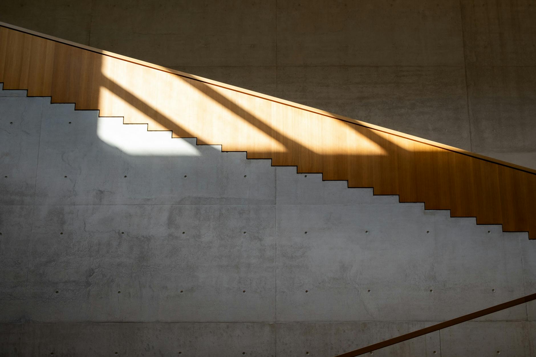 A minimalist staircase with sunlight casting geometric shadows on concrete walls.