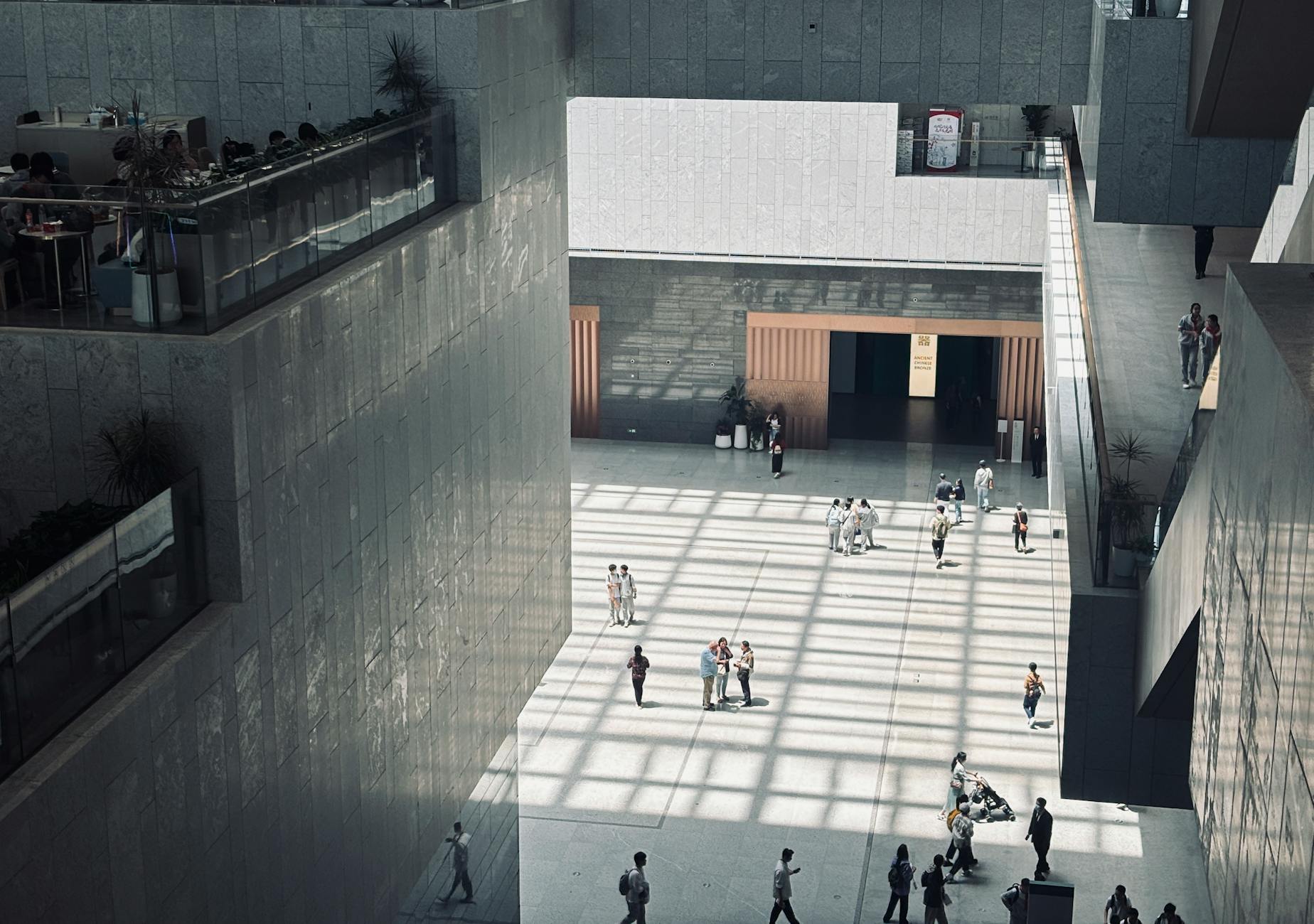 A spacious indoor atrium with geometric shadows and people walking by.