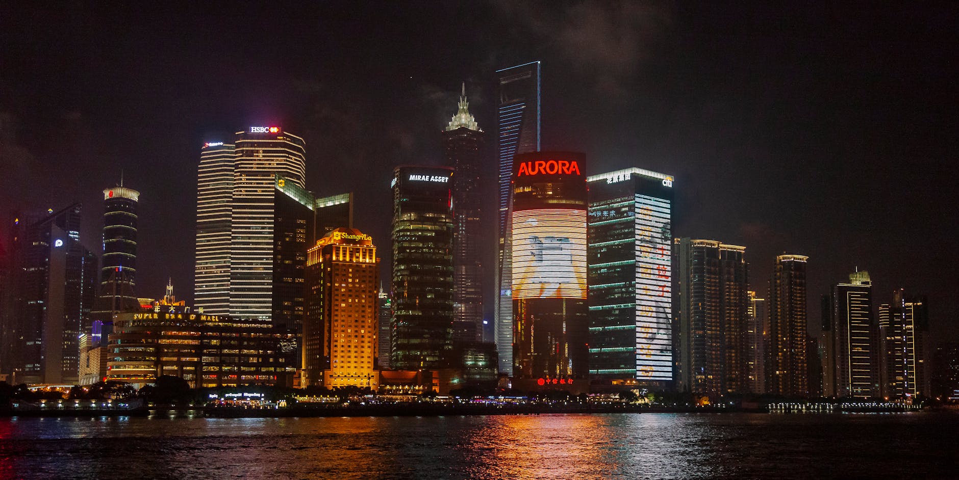 Contemporary multistage building exteriors with inscriptions near shiny rippled river in city at night