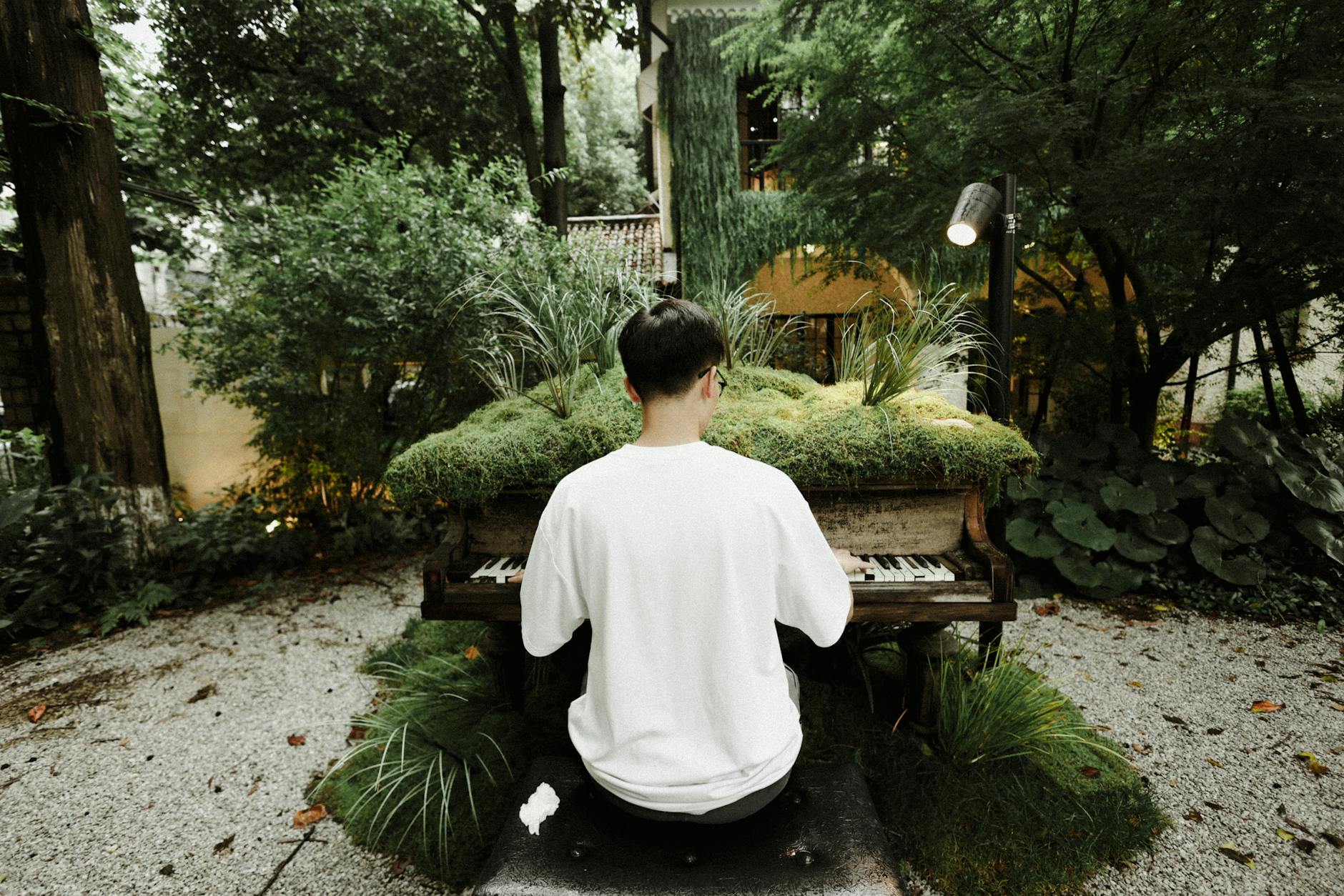 A man plays a grass-covered piano in a serene outdoor garden setting in Shanghai.