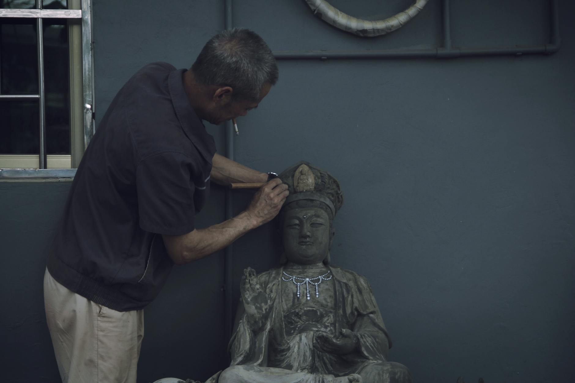 Man carefully restoring an antique Buddha statue indoors, focusing on details.