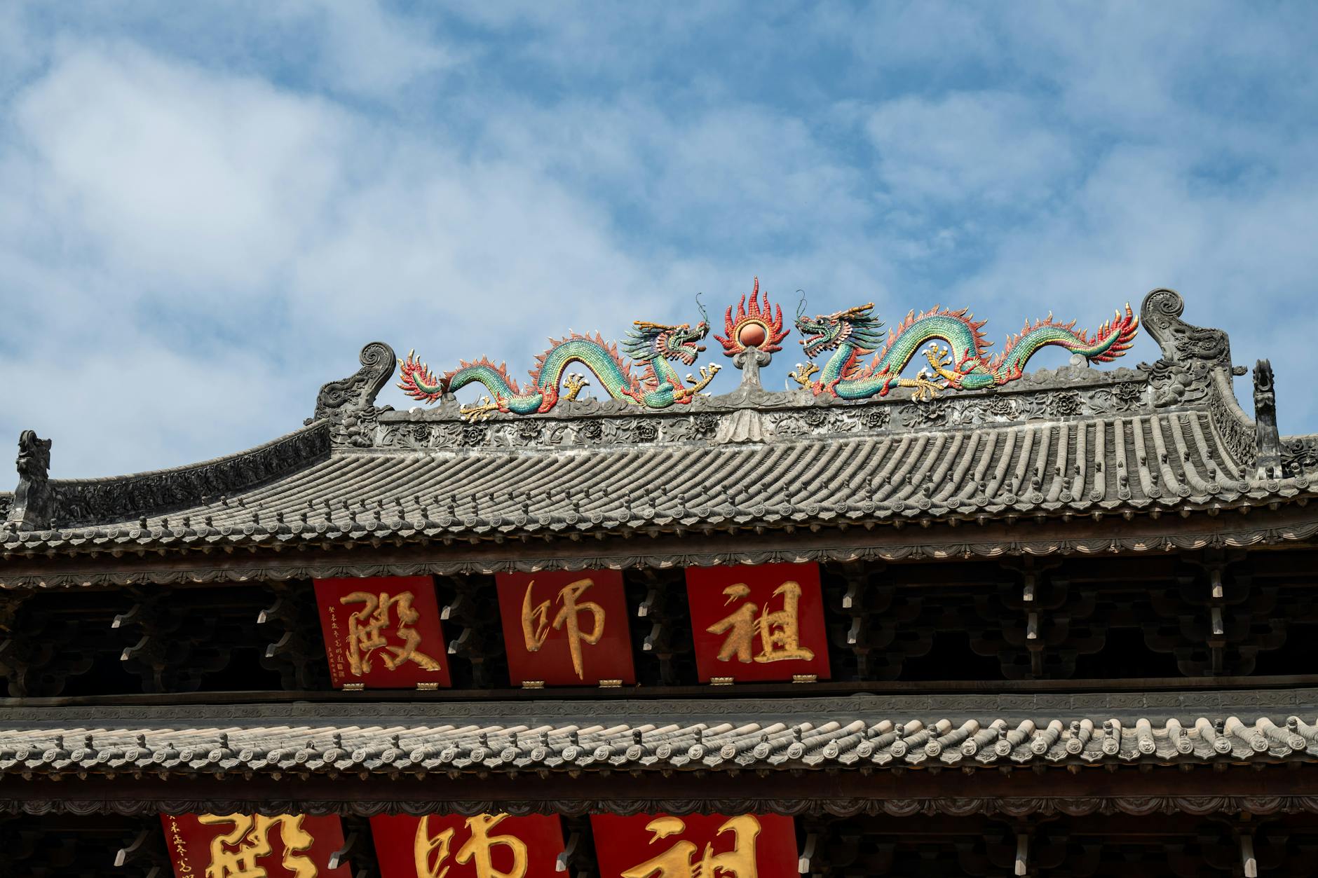 Ornate dragon sculpture atop an ancient Chinese temple roof with red banners, under a clear blue sky.