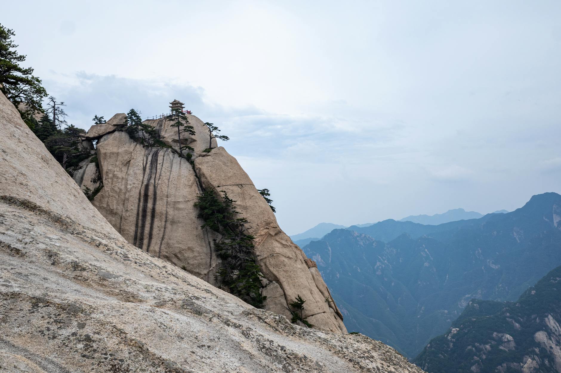 Breathtaking view of Mount Hua's rugged peaks with scattered vegetation under a cloudy sky.