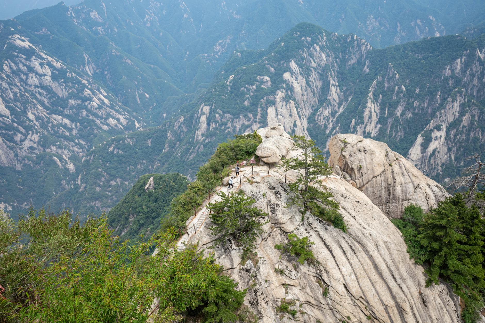 Breathtaking view from a rocky peak on Mount Hua, surrounded by lush greenery and rugged cliffs.