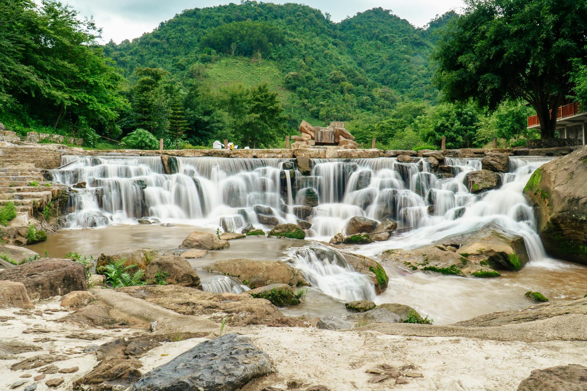 Beautiful waterfall flowing over rocks with lush green hills in Vietnam.
