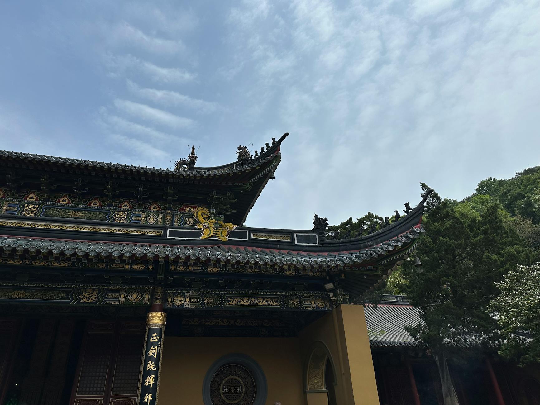 Elegant traditional Chinese temple roof with intricate designs surrounded by trees under a vibrant blue sky.