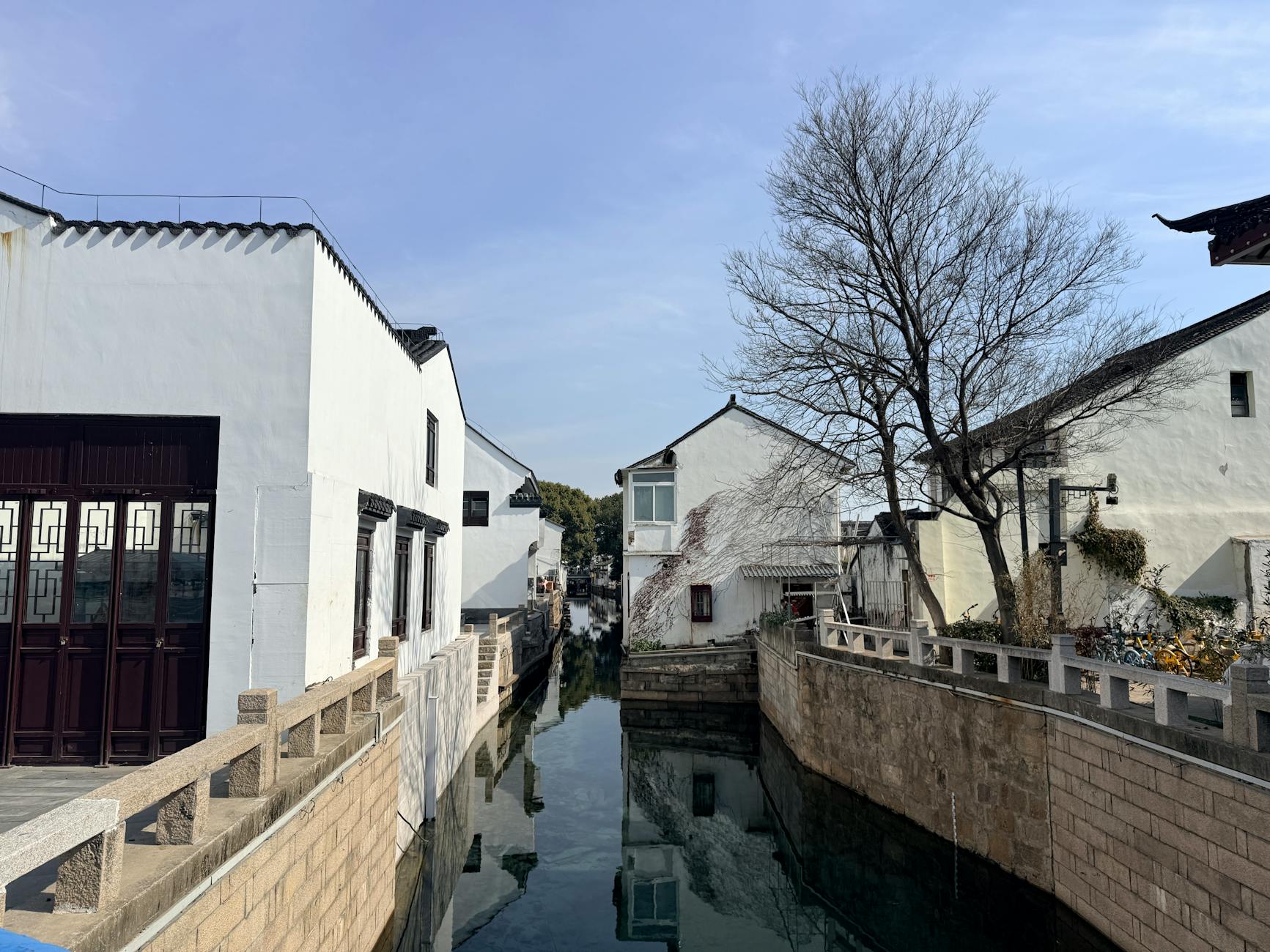 Charming view of traditional whitewashed houses by a calm canal in Suzhou, China, on a sunny day.