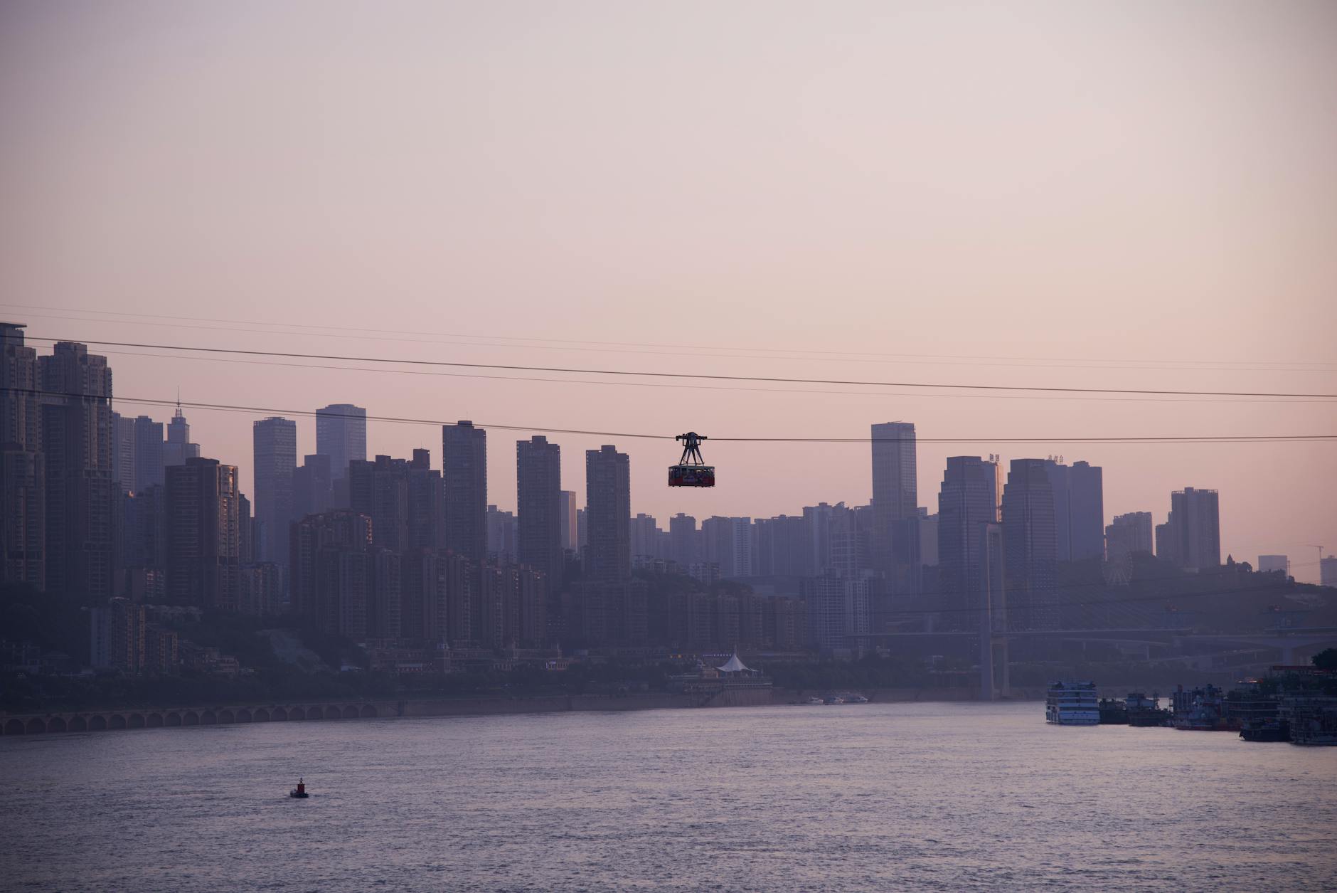 Silhouette of Chongqing skyline with cableway crossing the Yangtze River during sunset, offering urban scenic view.