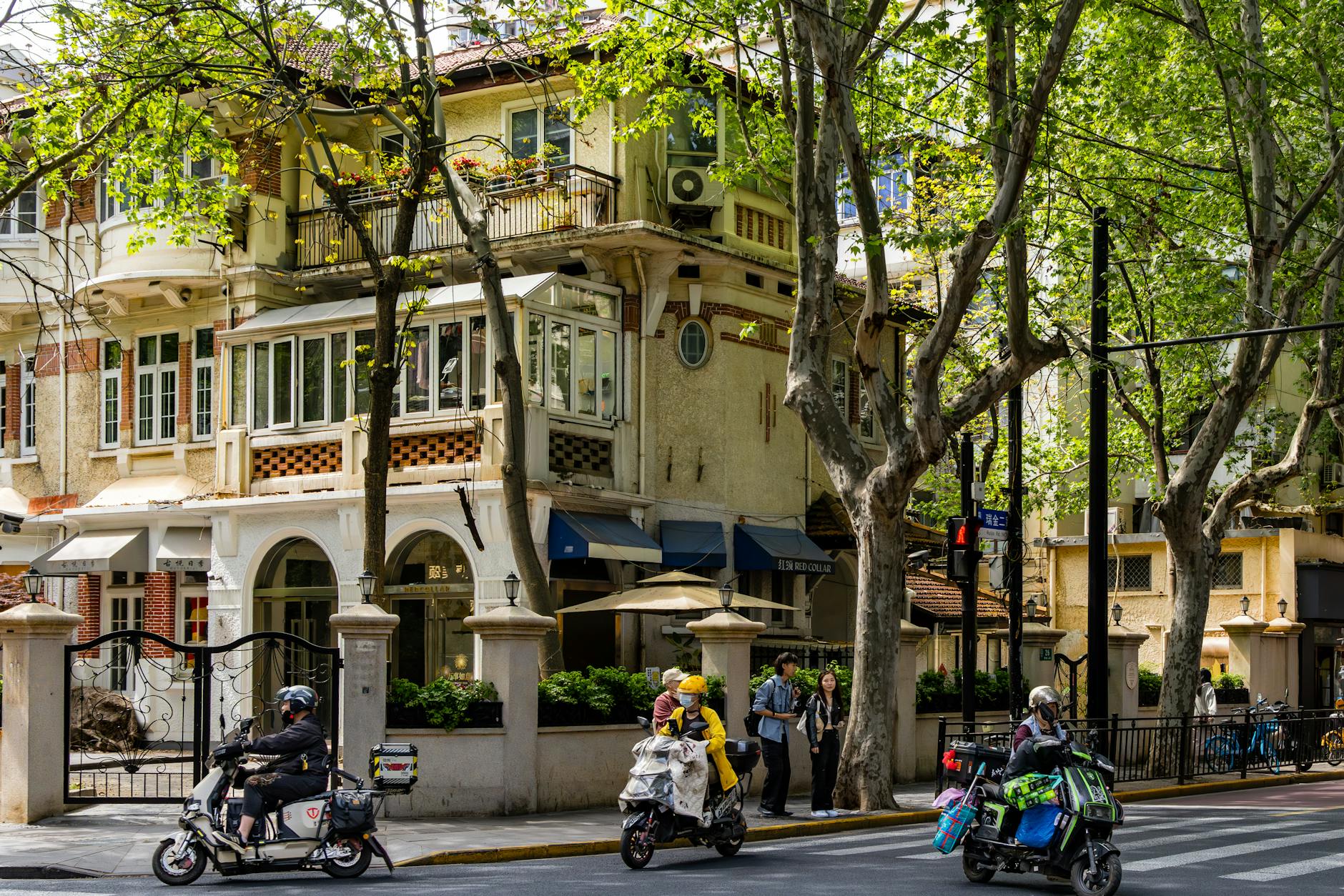 Historic European-style building with scooters on leafy Shanghai street.
