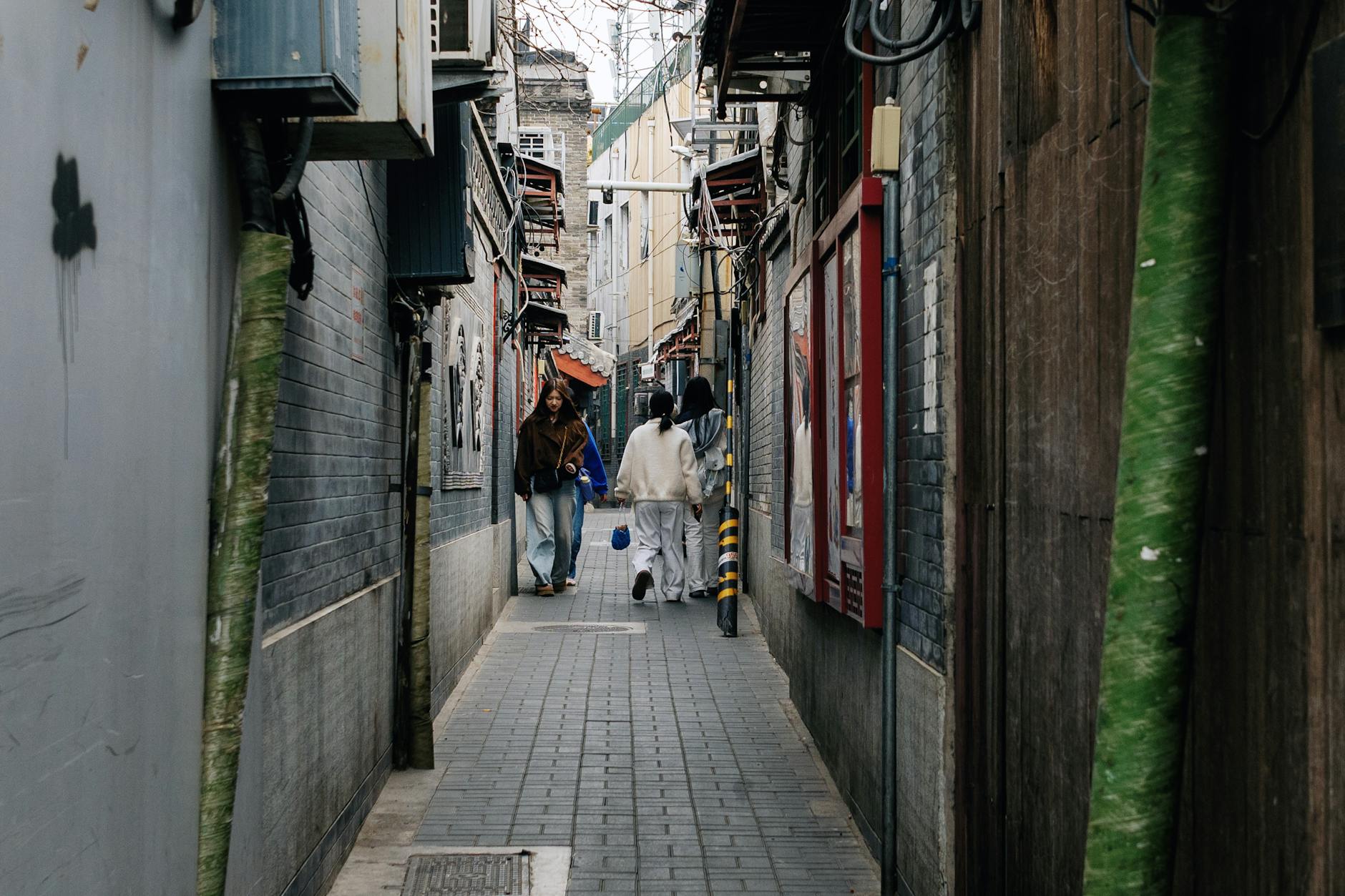 Image of a narrow alleyway in Beijing with people walking, showcasing urban life in China.