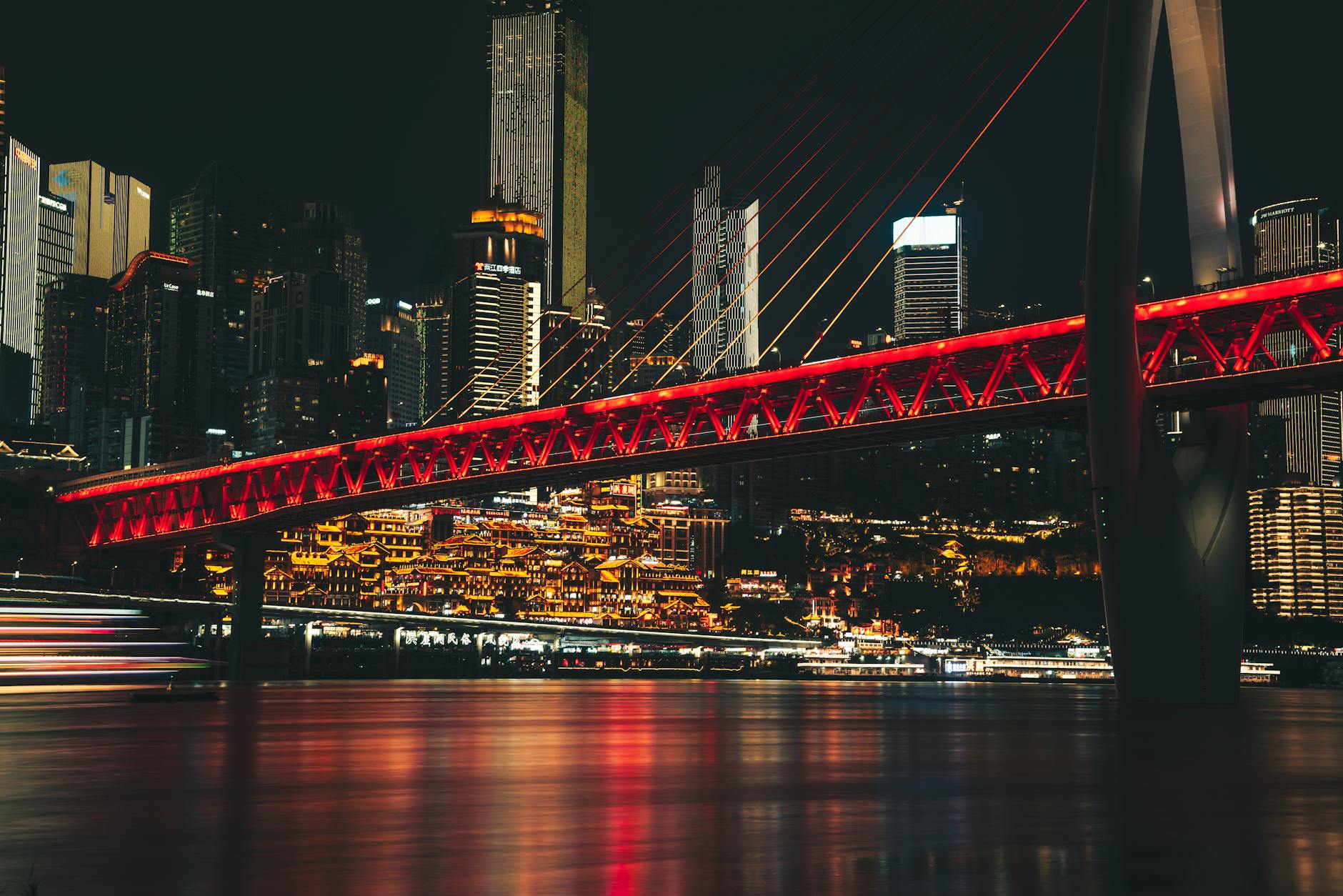 Stunning night view of Chongqing with illuminated bridge and city lights reflecting on water.